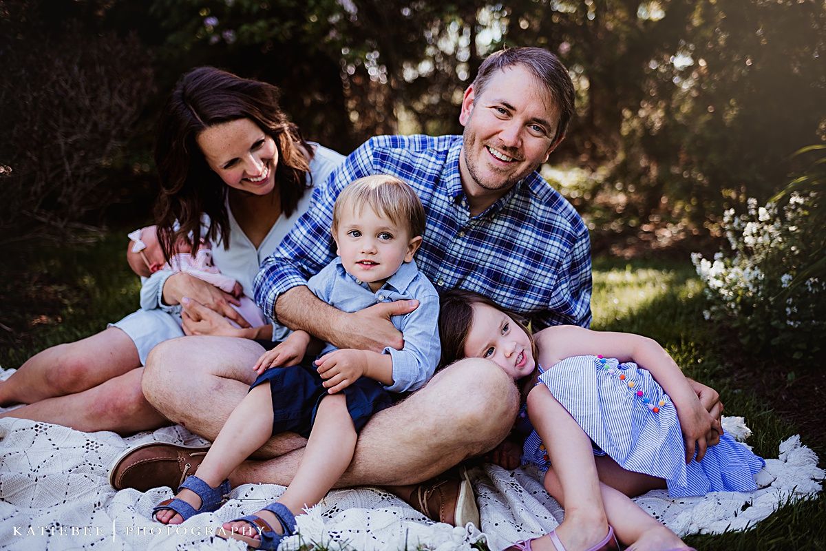 Joyful family portrait on a blanket outdoors with matching blue clothing.