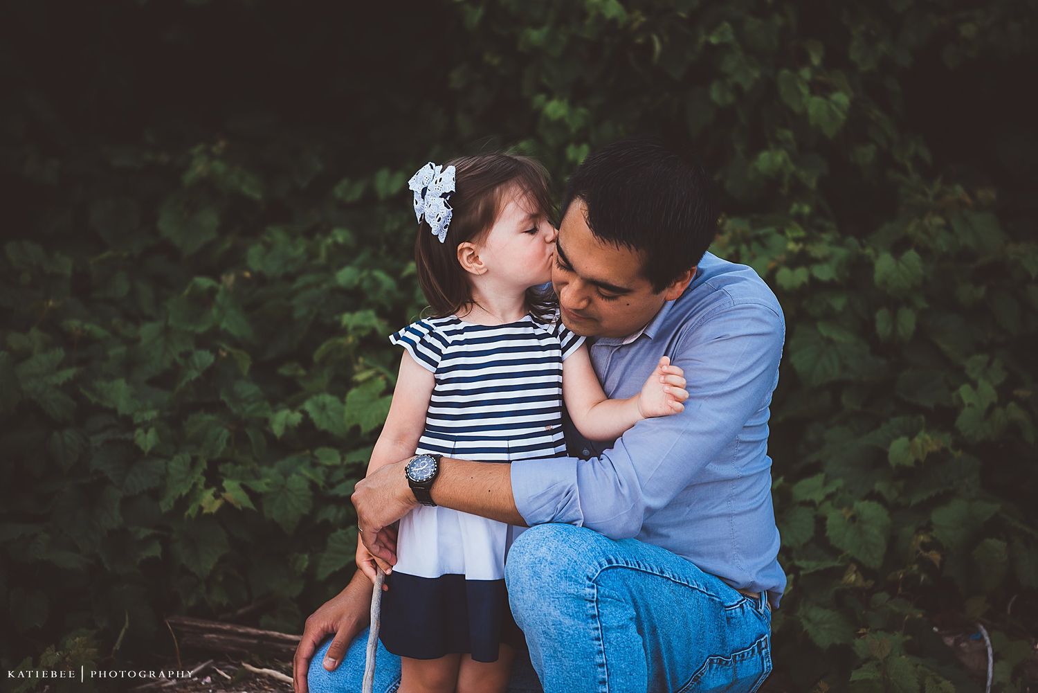 A tender moment shared between parent and child embracing outdoors against a leafy green background.