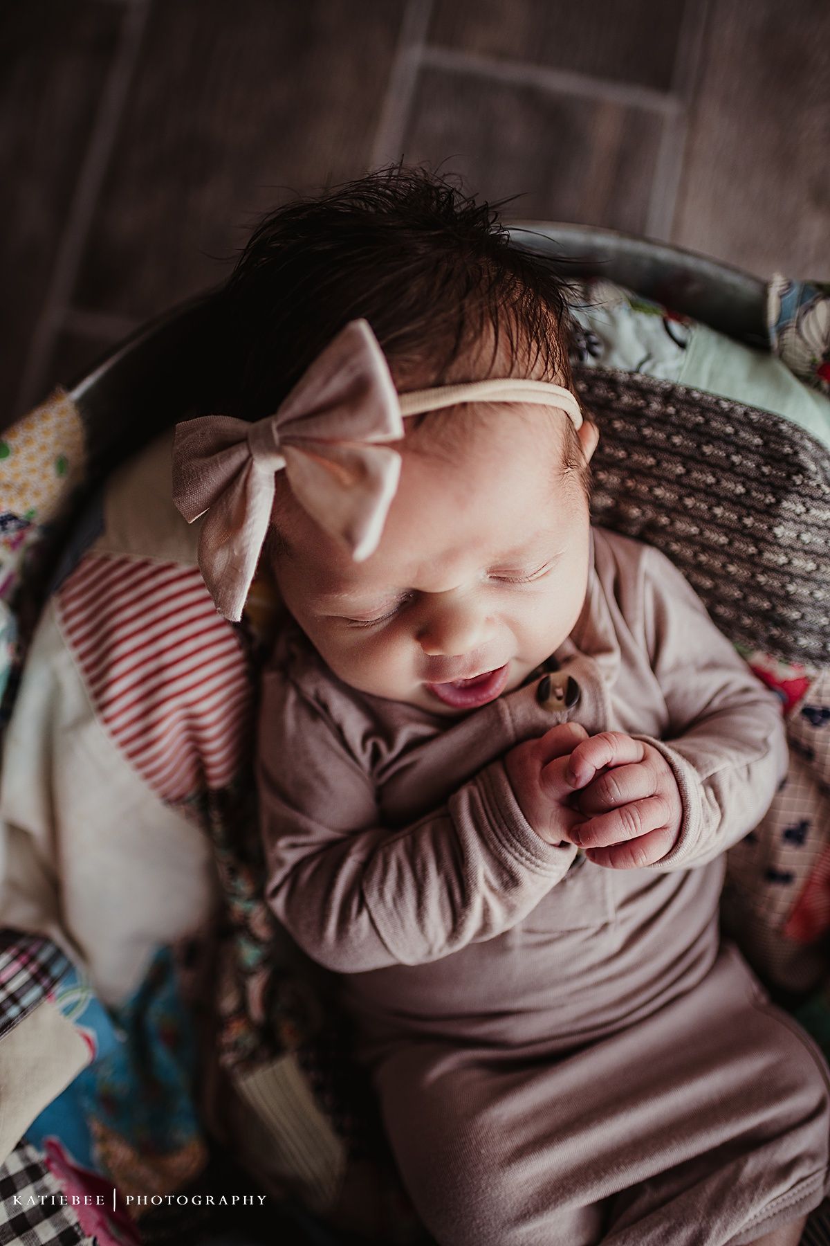 Peaceful sleeping baby in beige outfit with pink bow headband on textured blanket.