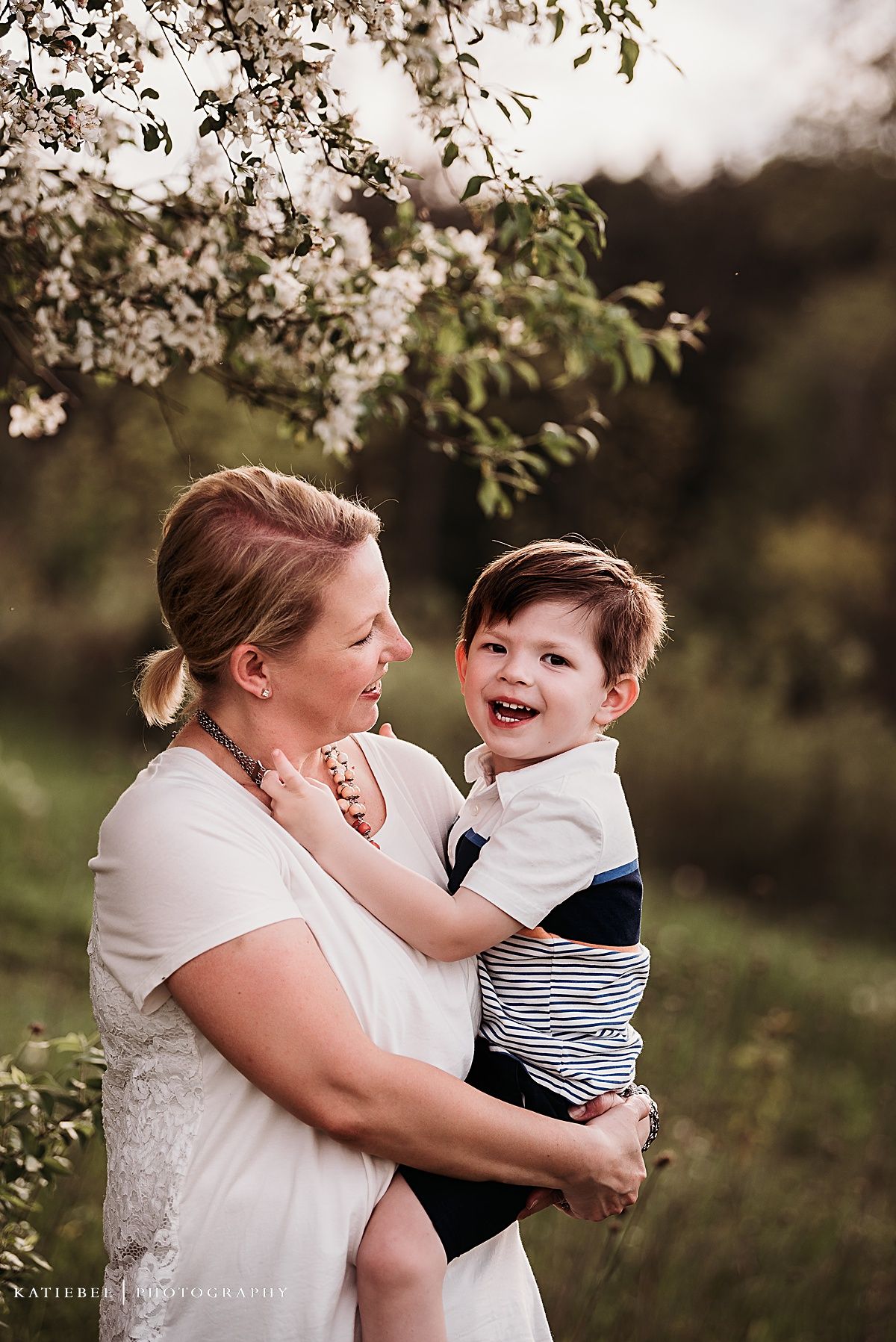 A tender moment between parent and child under blooming spring tree branches.