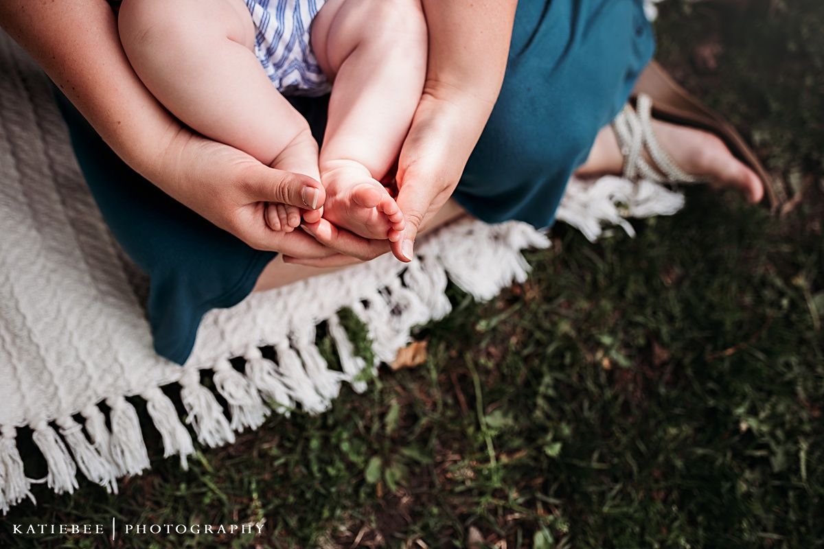 Detail shot of tiny feet resting on a white blanket with tassels against grass.