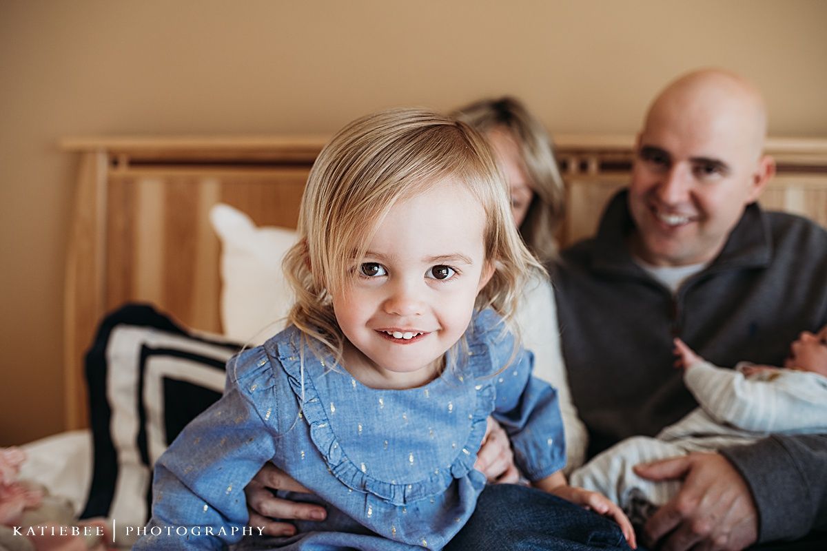 A candid family moment captured in a bedroom with natural lighting and wood furniture.
