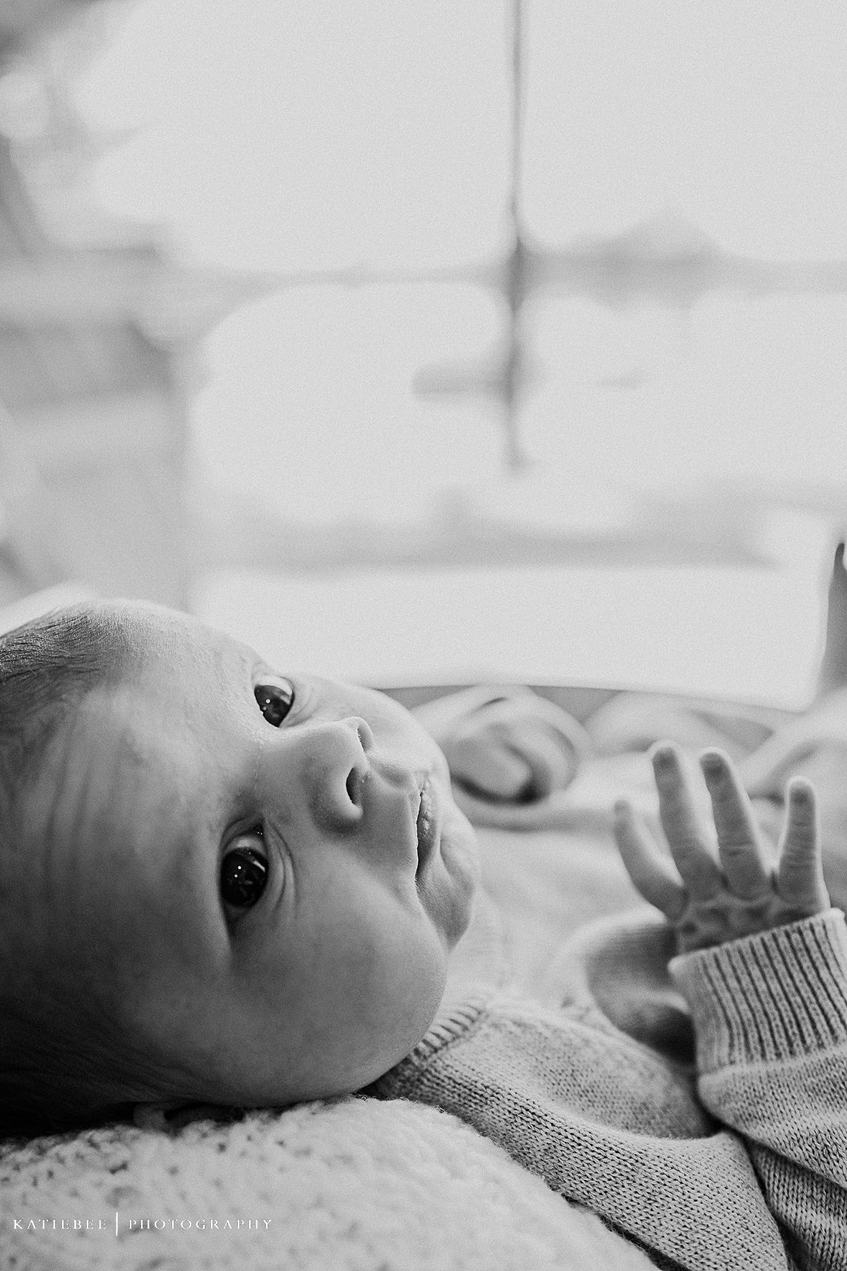 Close-up black and white portrait of baby lying on soft surface.