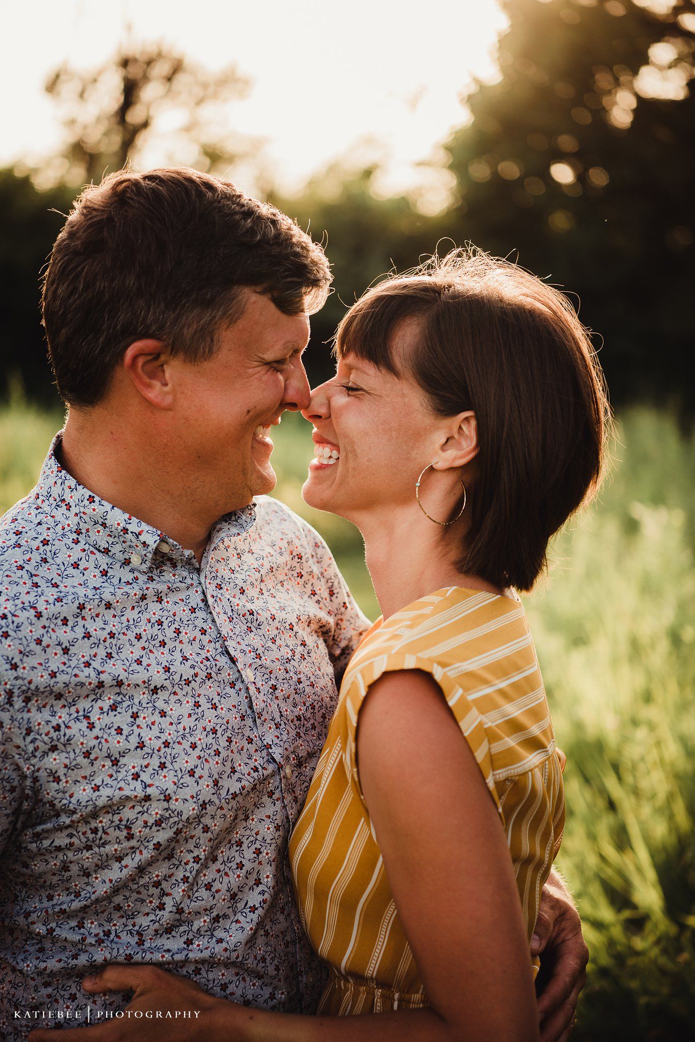Couple sharing a romantic laugh together at sunset in a grassy field.