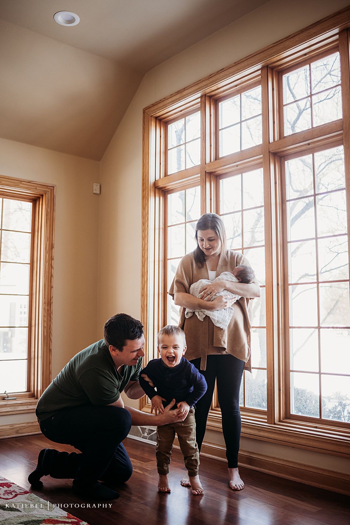 Family shares playful moment together by large windows with natural light streaming in.