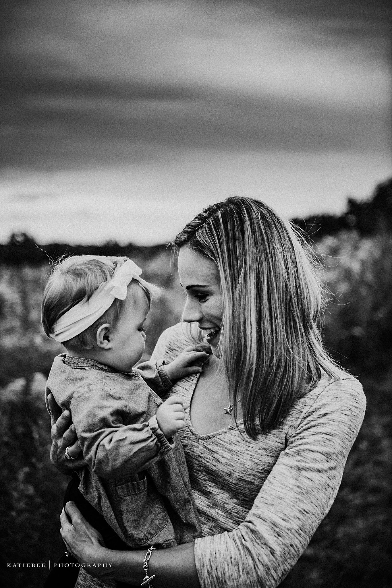 Sweet emotional black and white portrait of mother and baby bonding in a field at sunset.