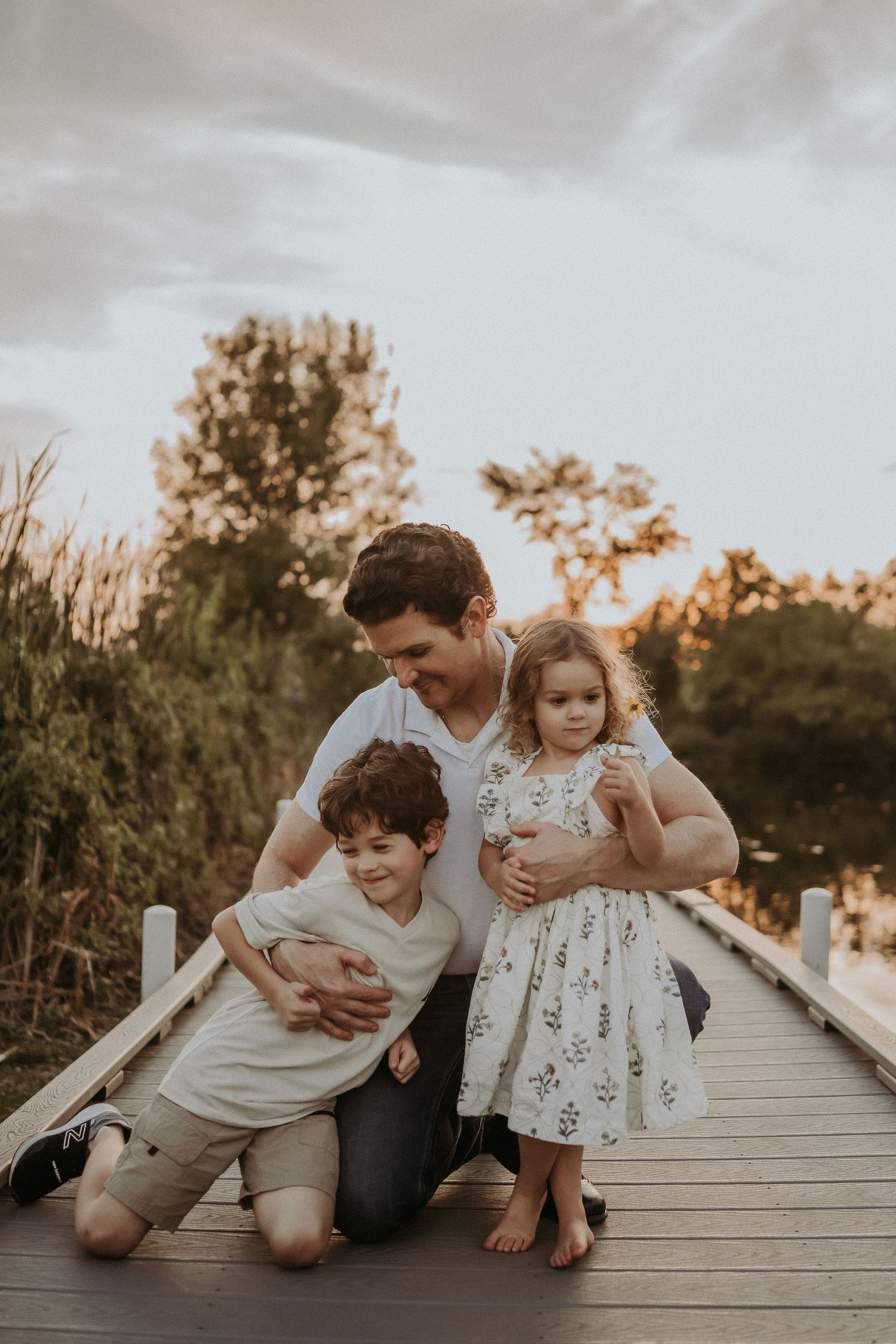 Candid family moment showing playful interaction on a wooden dock at sunset.