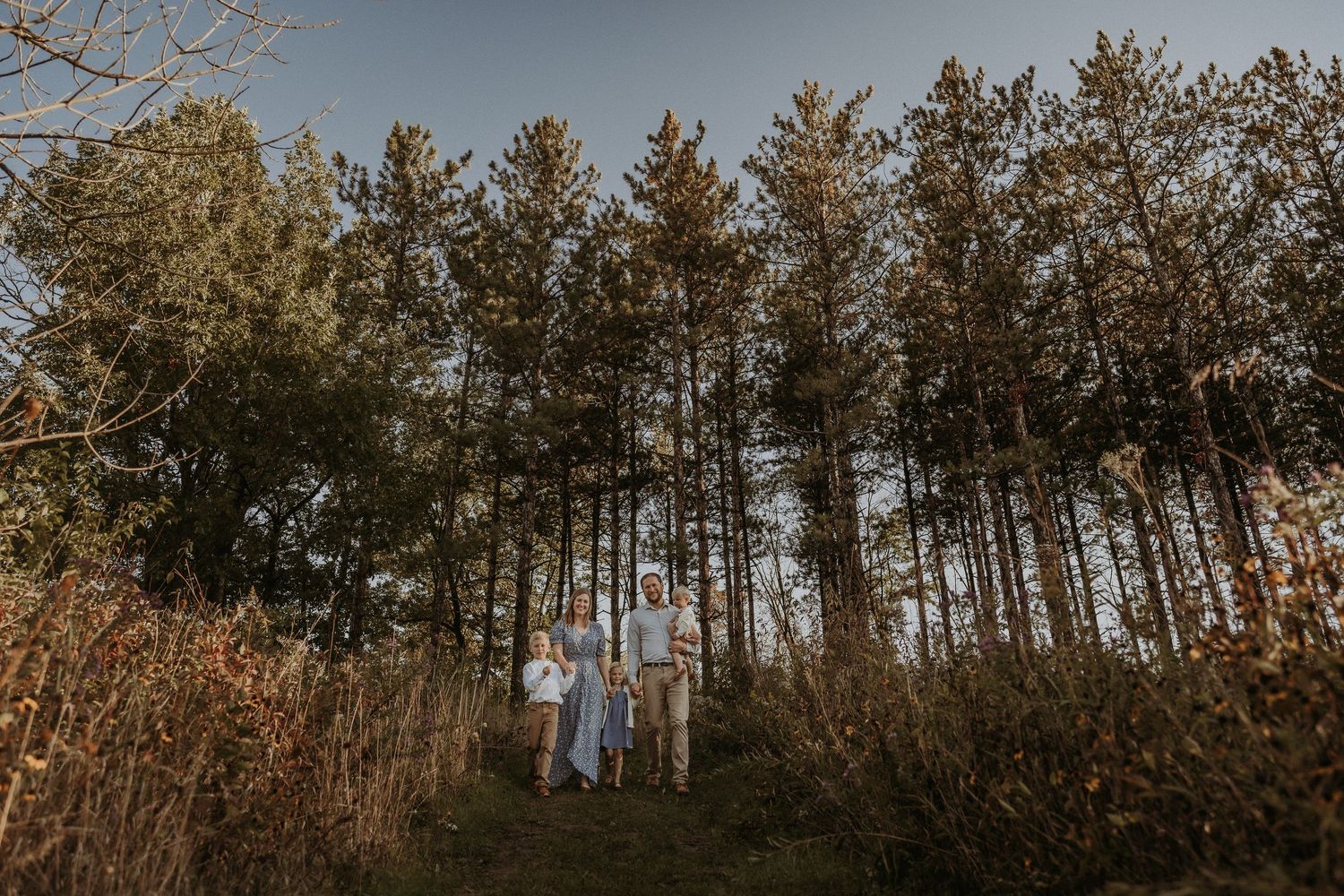 Group standing together among tall pine trees at golden hour in a natural outdoor setting.