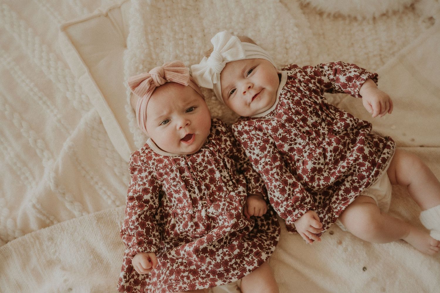 Two infants in matching floral outfits resting on white blankets.