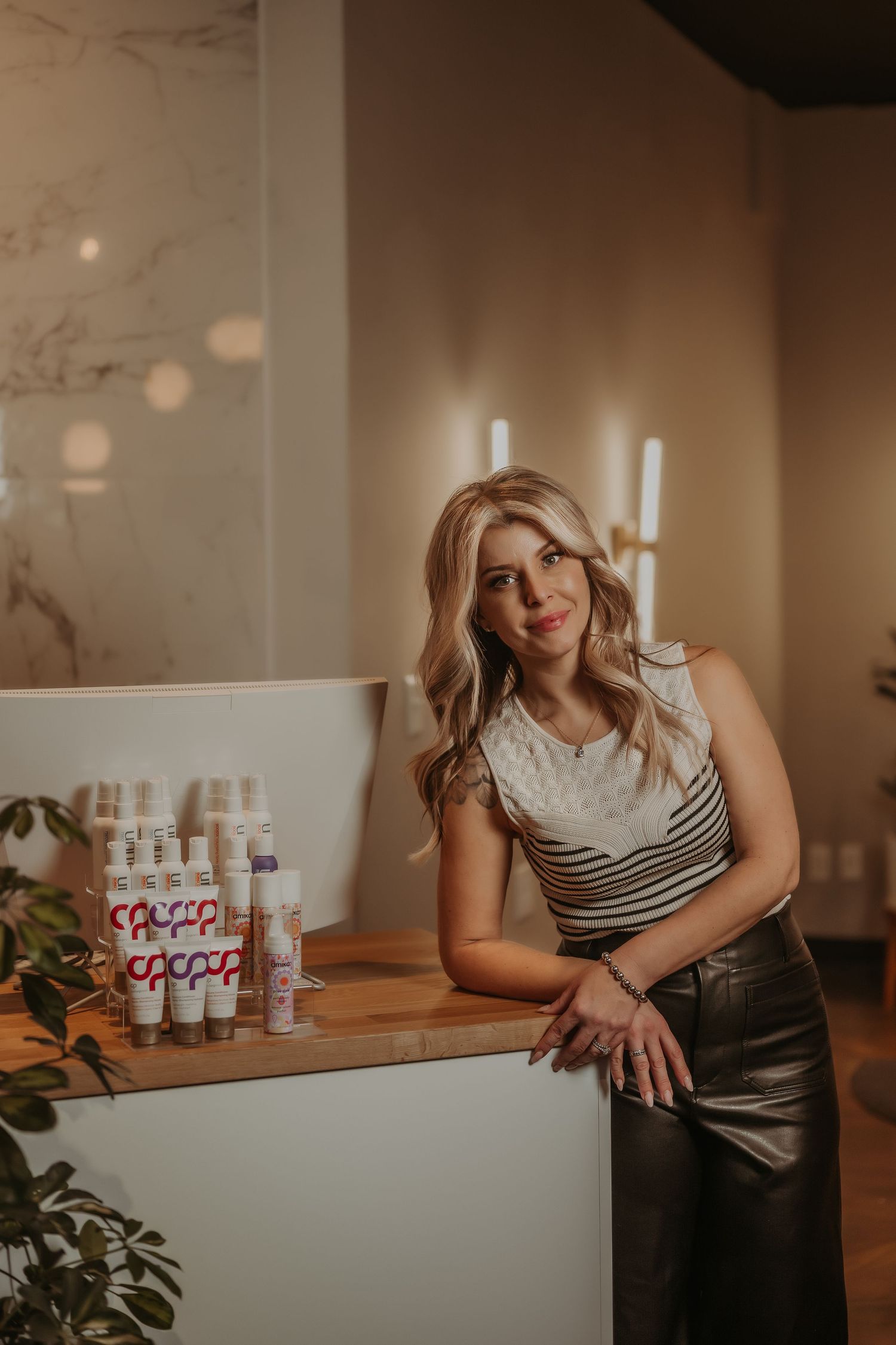 Professional lifestyle photo of woman in striped top leaning against counter with products displayed.