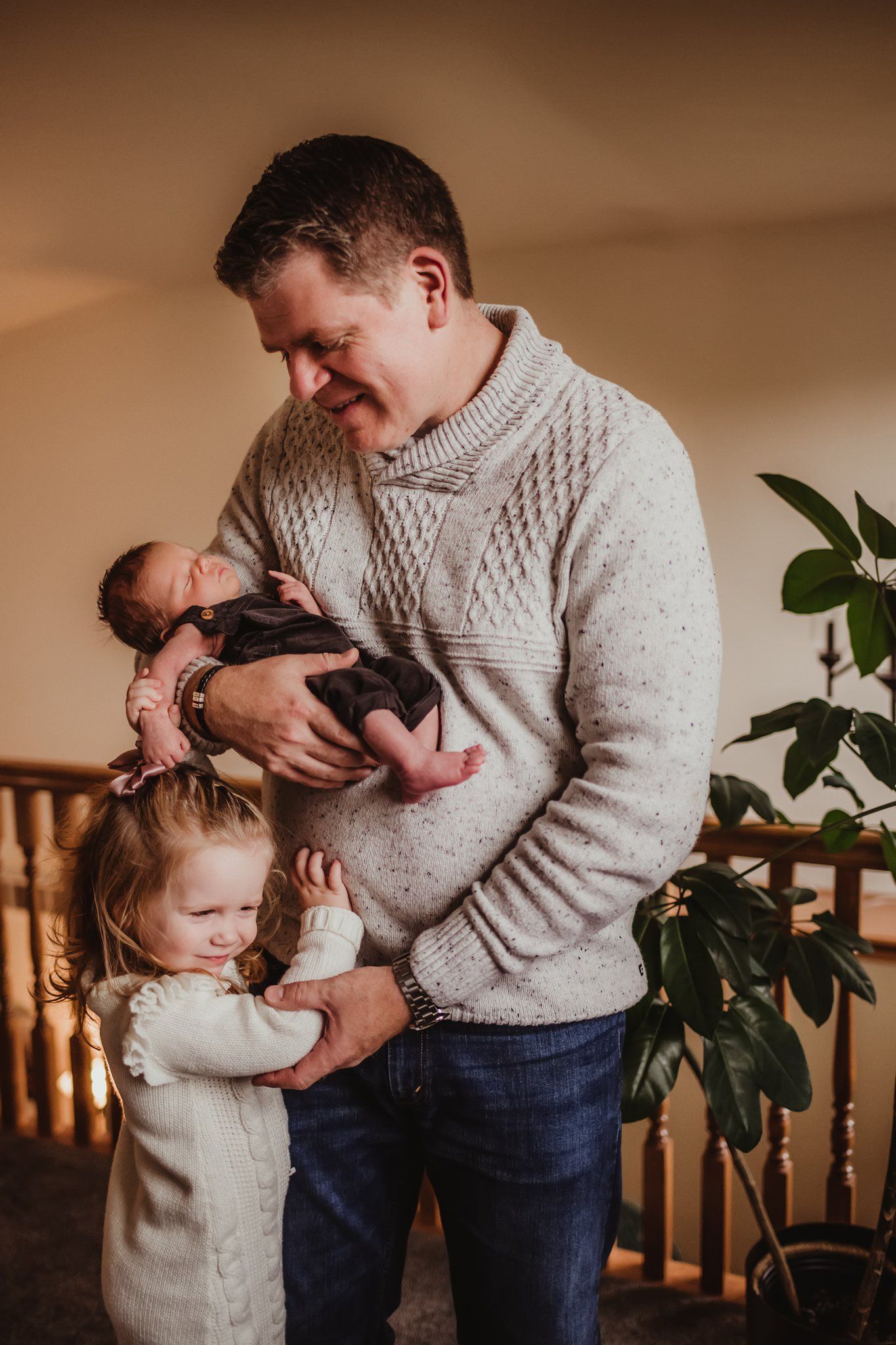 A touching family moment showing an embrace between parent, toddler, and newborn in a cozy home setting.