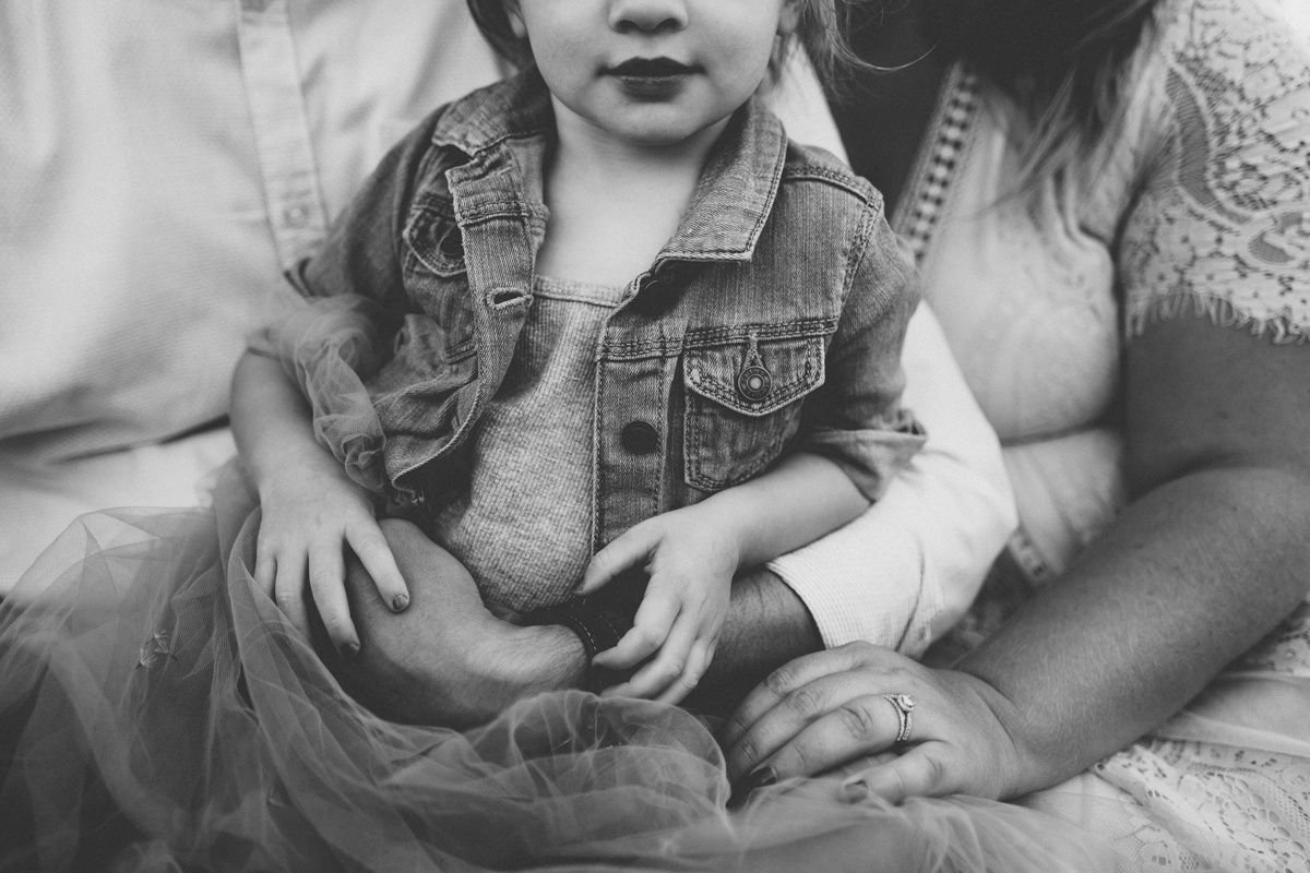 Close-up black and white photo of a small child wearing a denim jacket sitting with an adult.