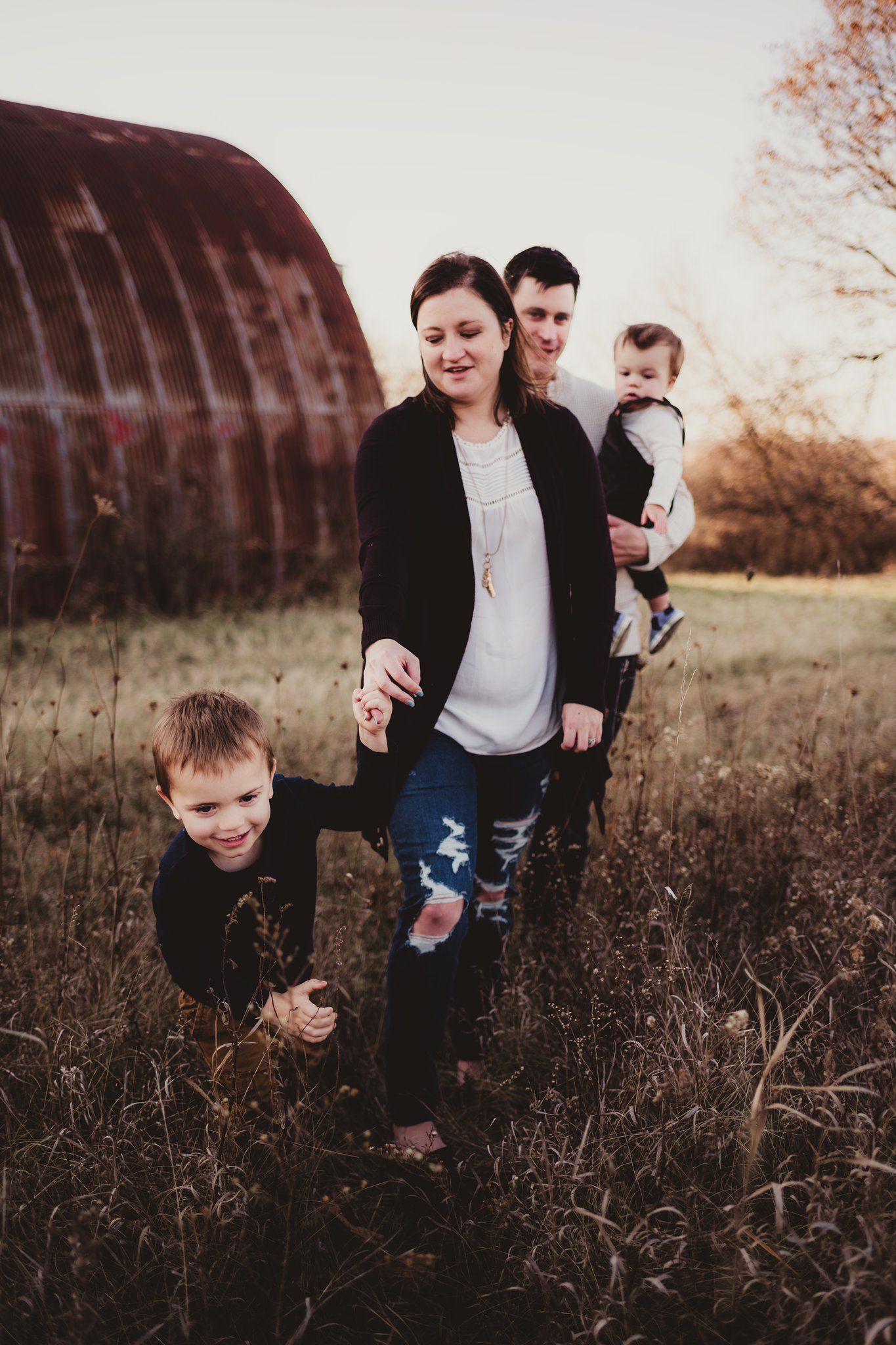 Casual family portrait outdoors with rustic red barn in background during golden hour.