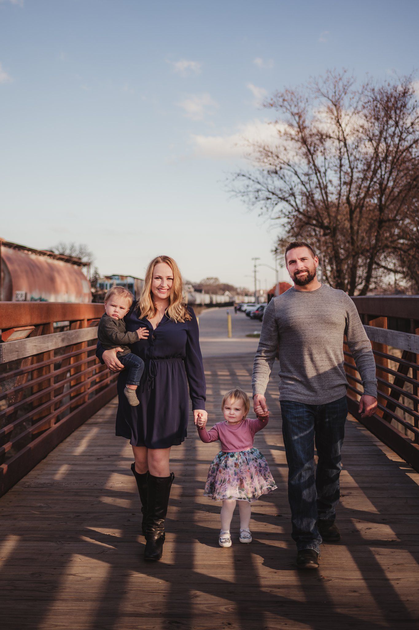 Family walks hand in hand across wooden bridge during golden hour.