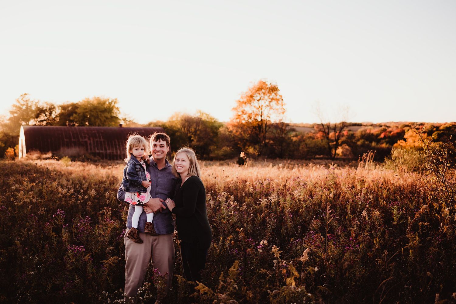 A family portrait captured in warm sunset light among tall autumn grasses.