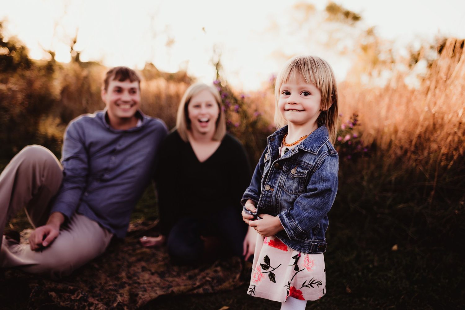Three people sit together in golden sunlight surrounded by autumn grass.