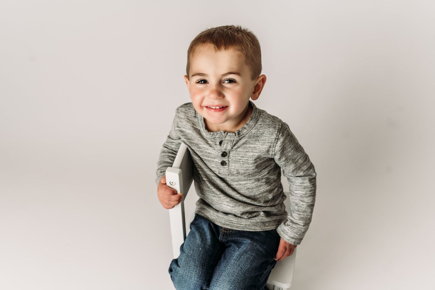 Energetic child in casual wear poses playfully on white backdrop.