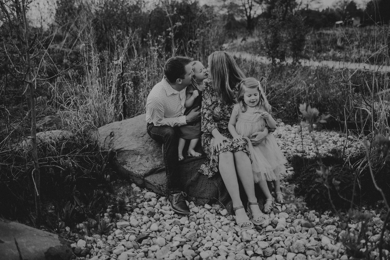 Black and white outdoor family portrait on rocky landscape with natural vegetation.