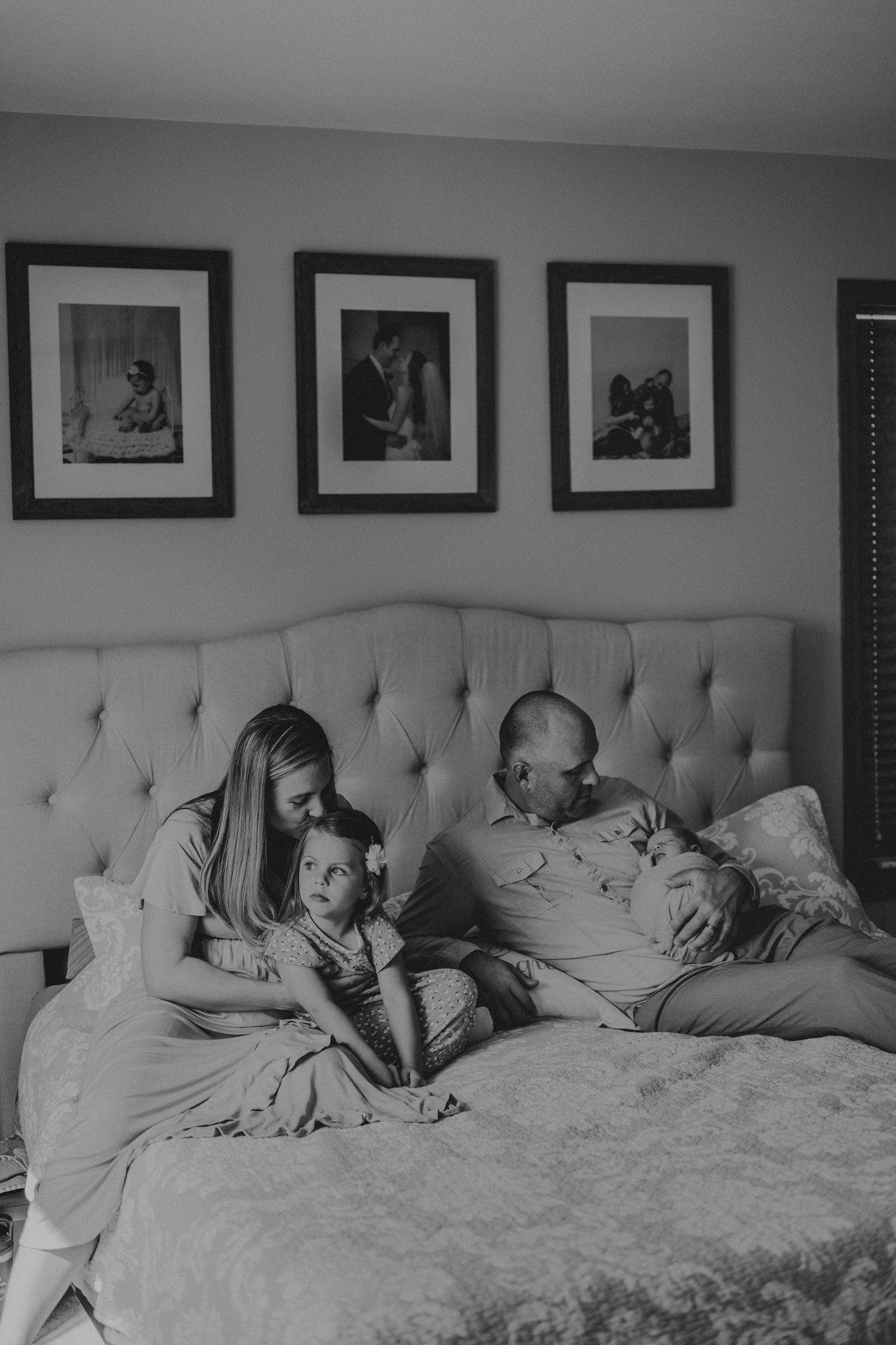 Black and white family portrait on bed with gallery wall above.