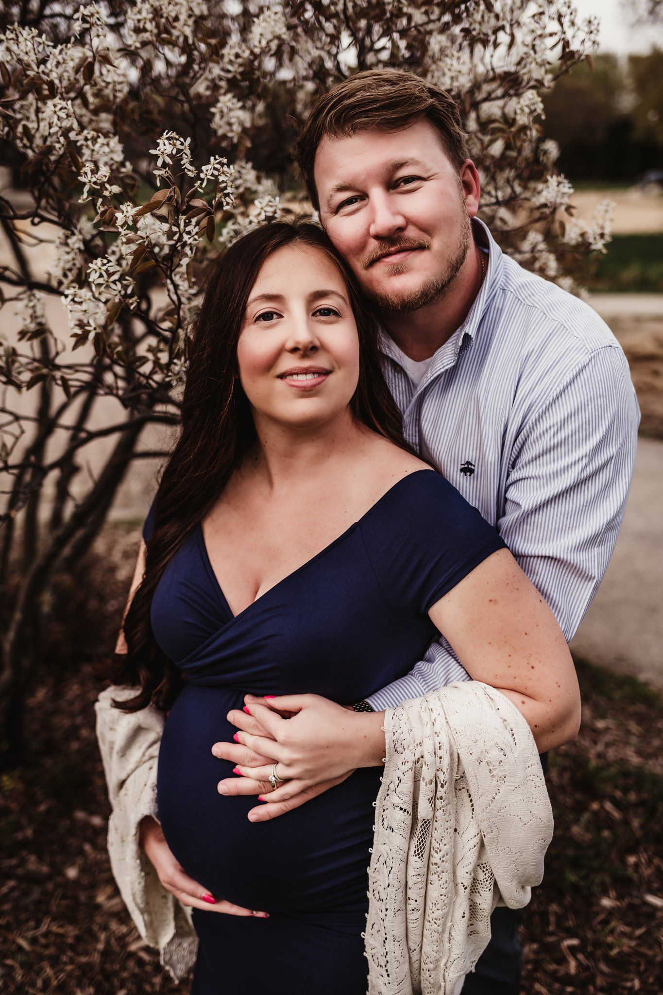 Intimate maternity portrait with couple embracing by flowering spring branches.