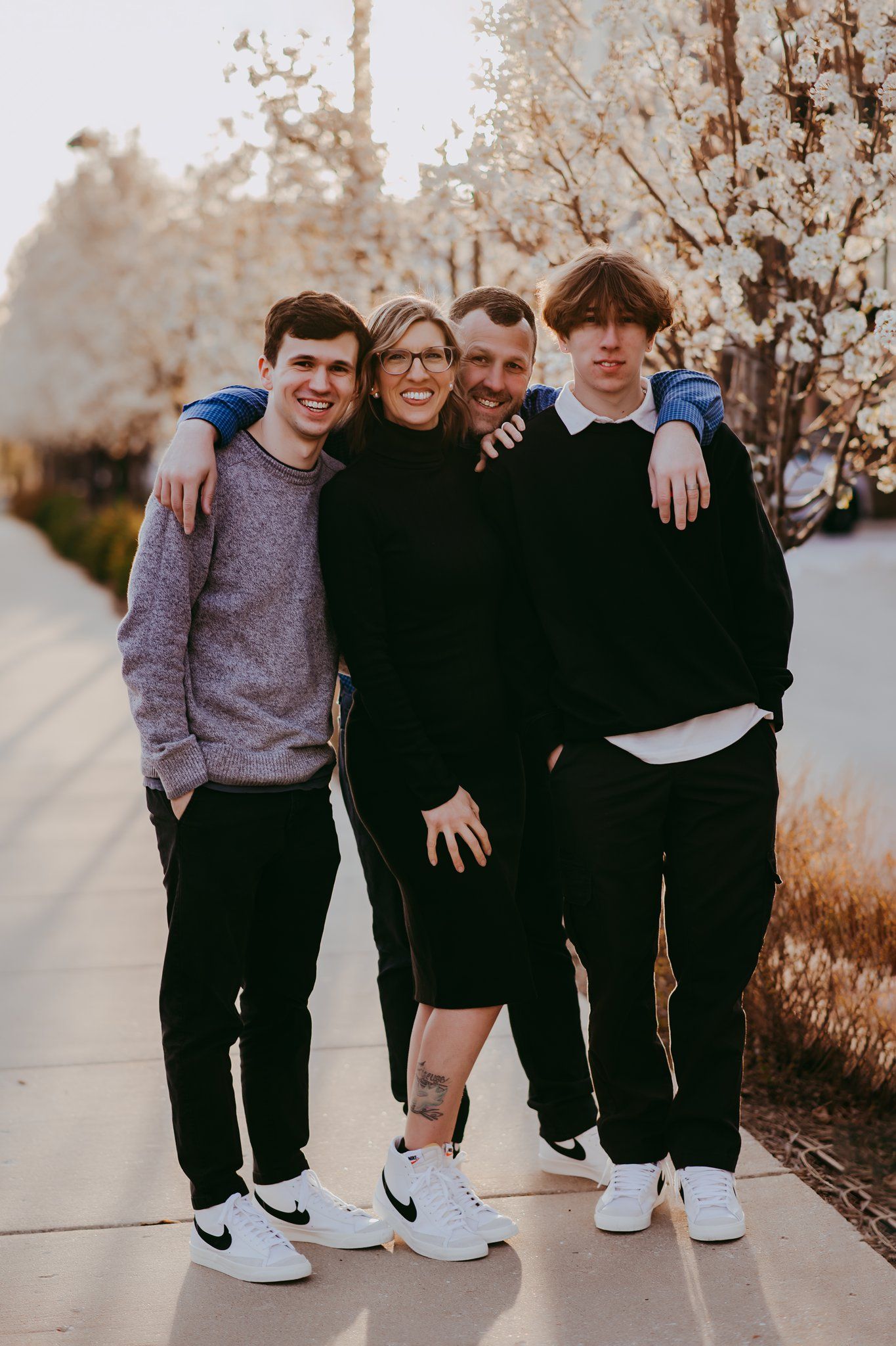 Group of four poses together on sidewalk wearing casual attire with blooming trees behind.