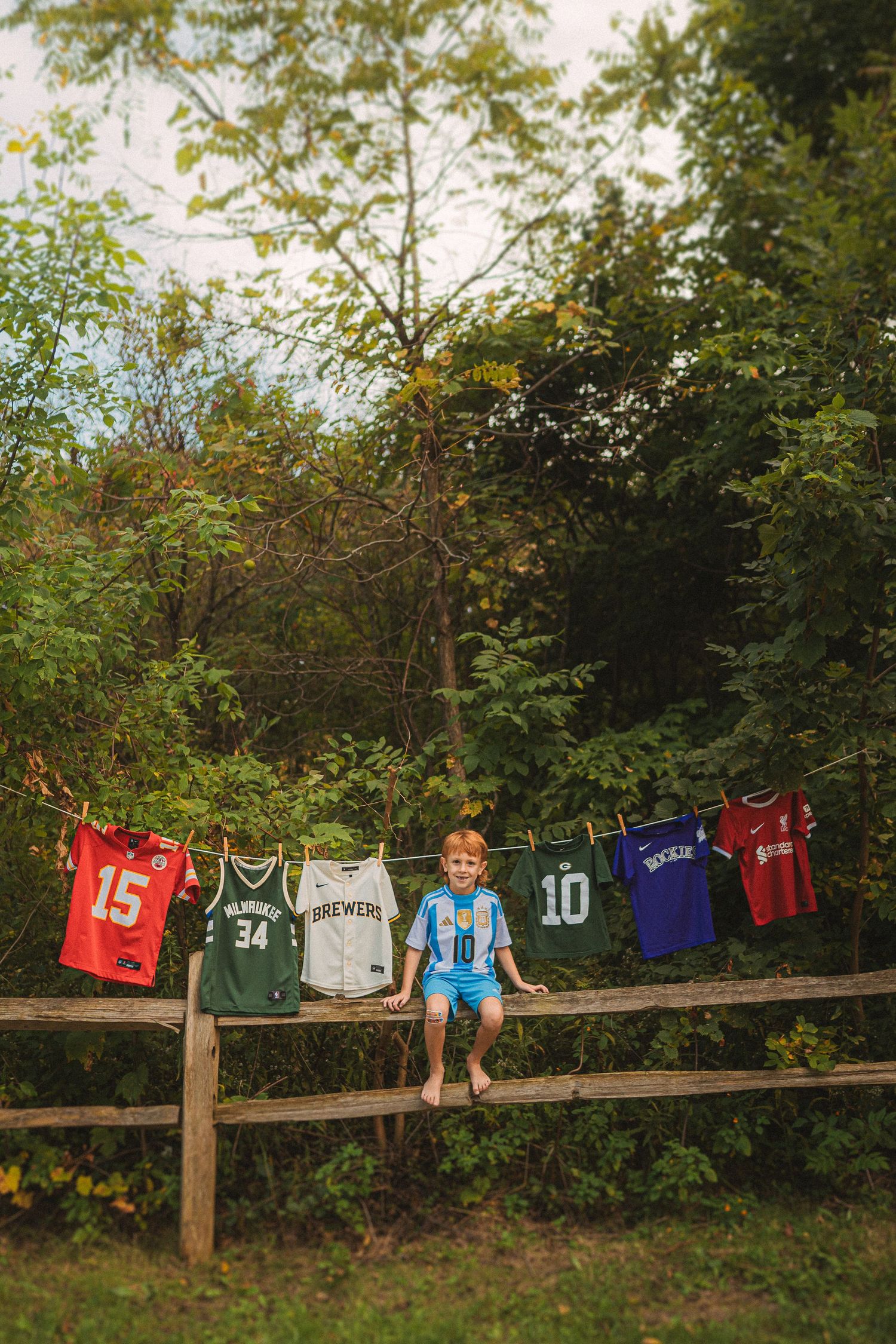Colorful sports jerseys displayed on a wooden fence with young person sitting between them.