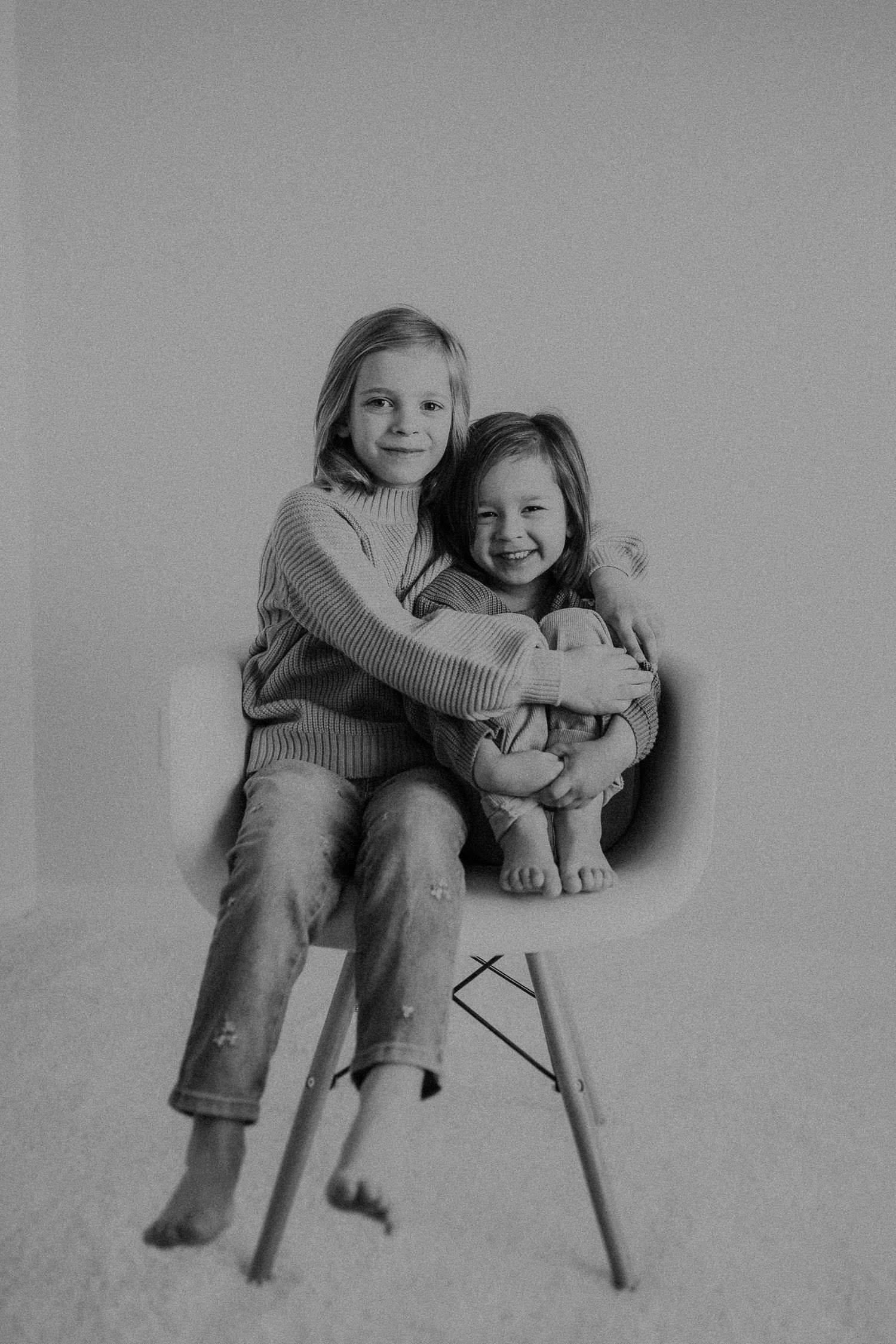 Two young people embracing while sitting together on a white Eames-style chair.