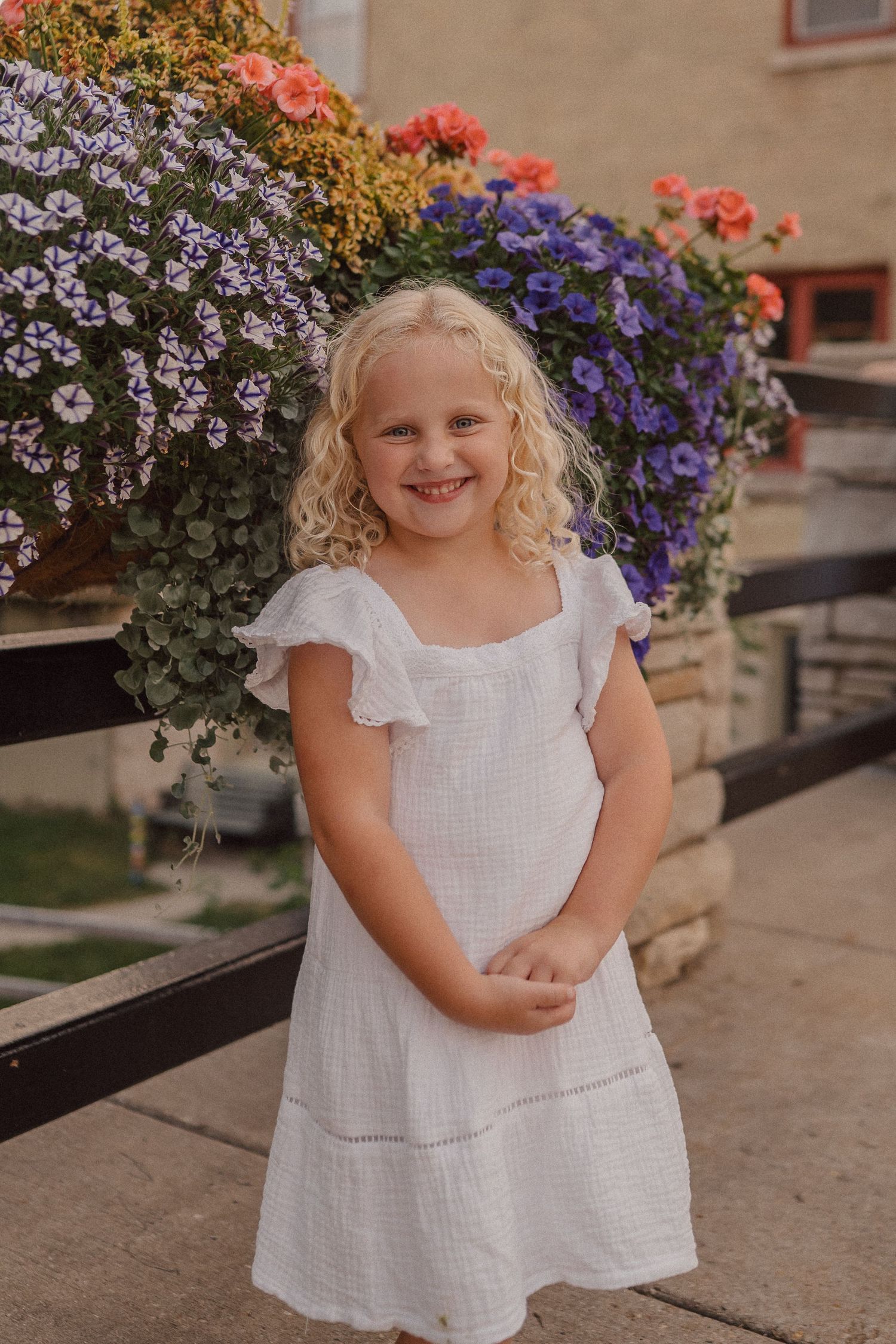 A white dress stands before a colorful flower display of purple, coral, and blue blooms.