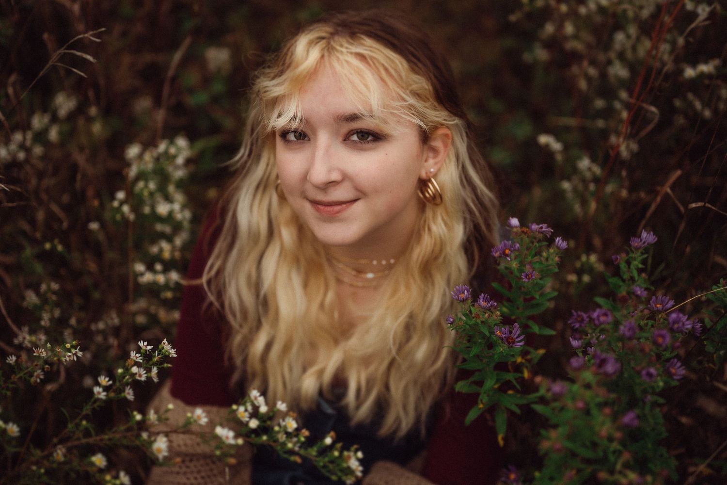 Whimsical portrait surrounded by blooming flowers and greenery with soft lighting.