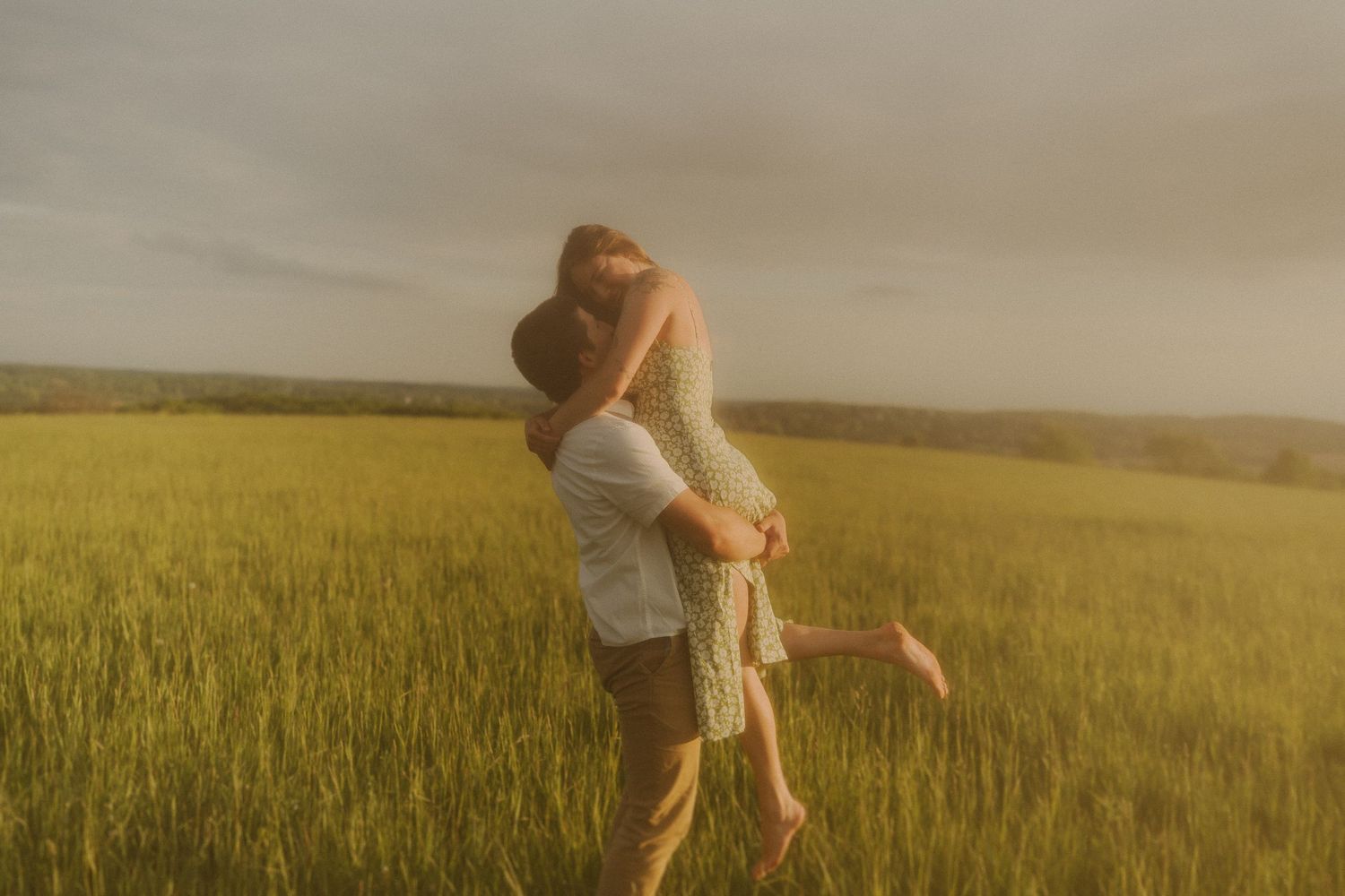 Playful couple running and twirling through tall wheat field during golden hour.