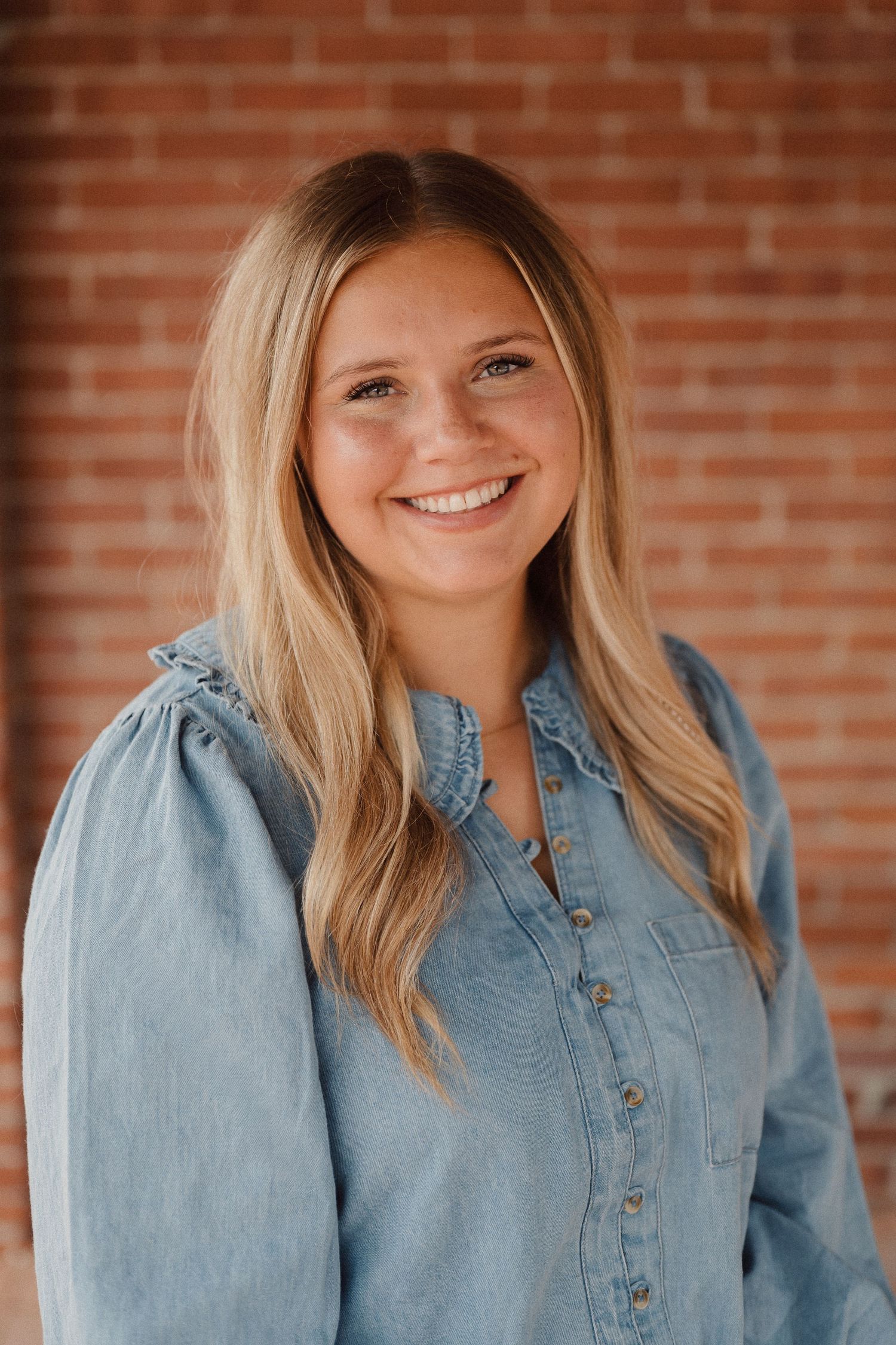 Blonde woman in light denim button-up shirt poses against brick wall in a sequence of connecting headshots.