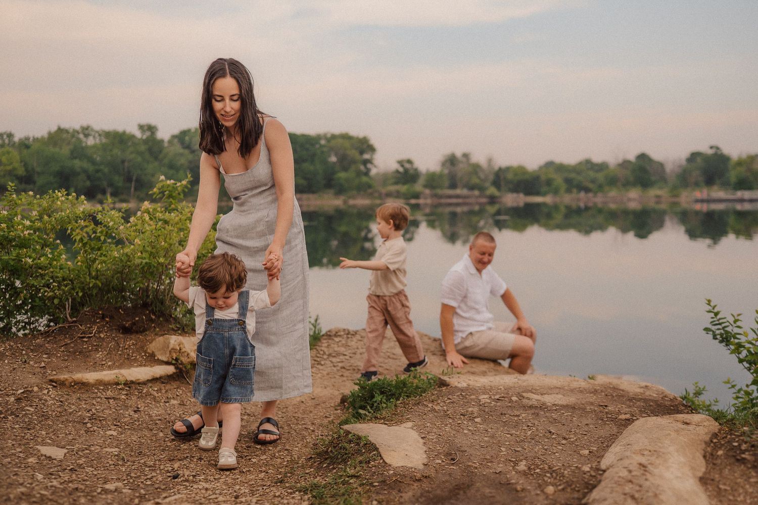 Family enjoying peaceful evening by lake shore with trees in background.