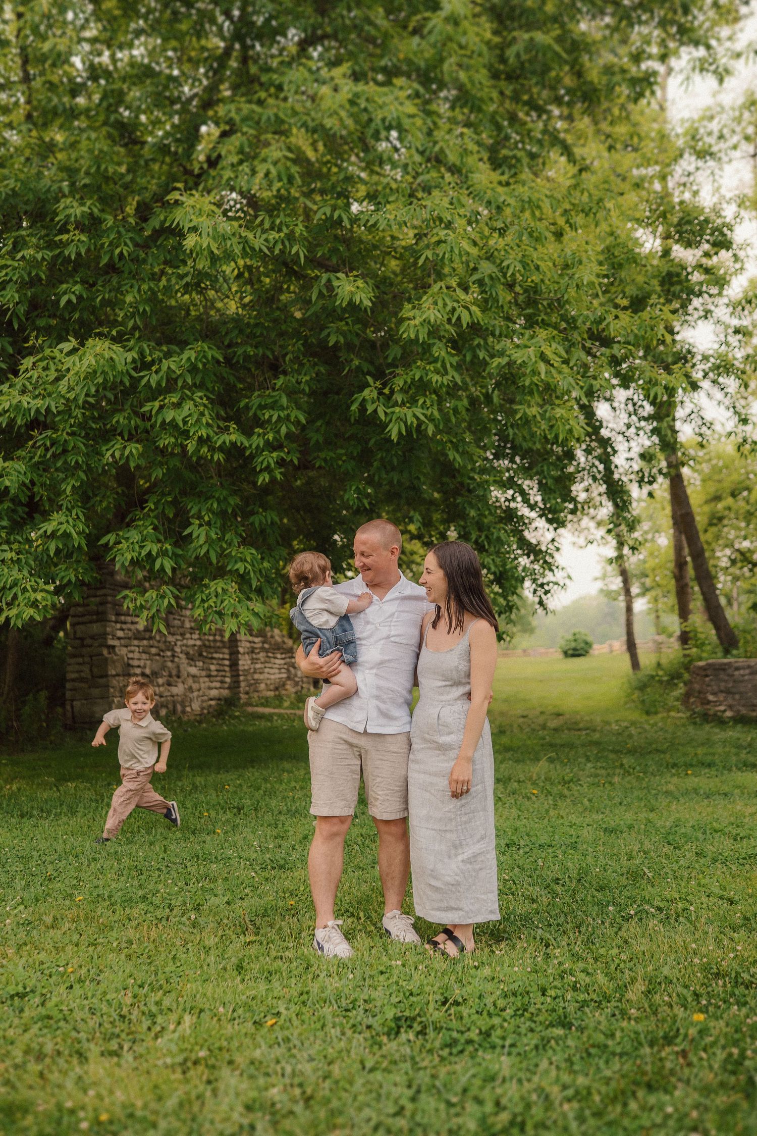 A family enjoying a summer day together in front of a stone wall and lush green trees.