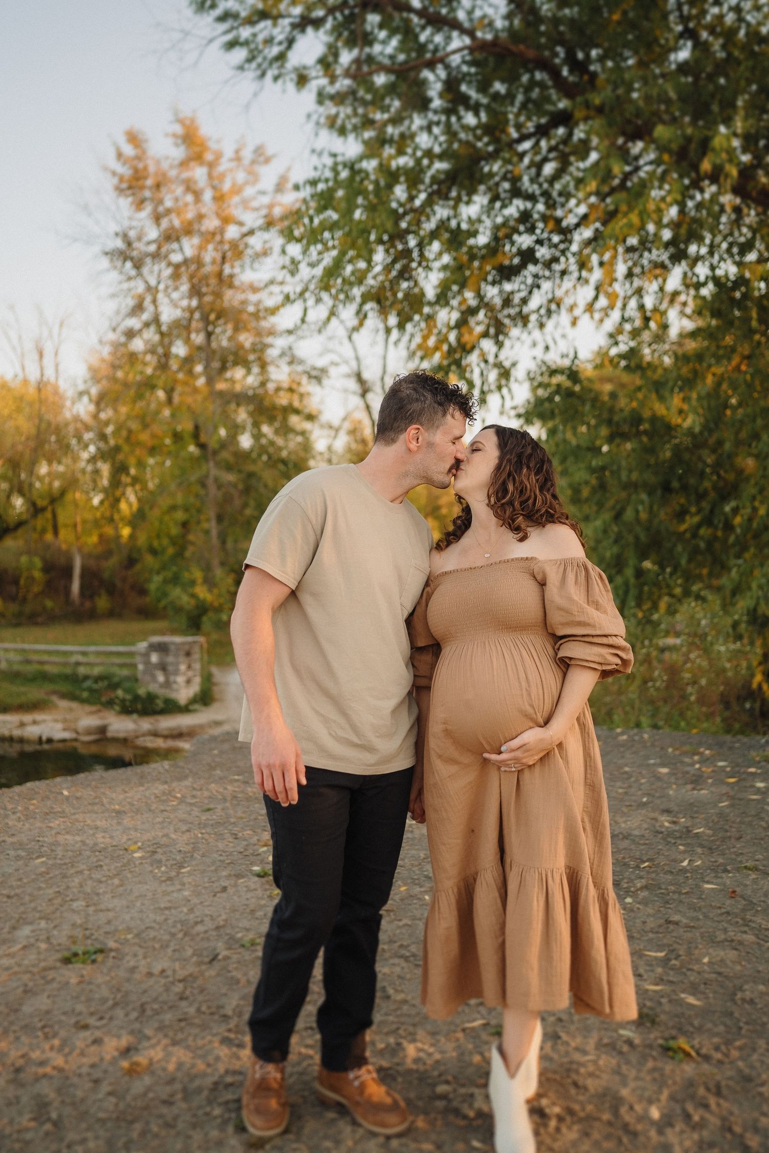 Intimate maternity moment captured in fall setting with warm natural lighting and earth-toned outfits.