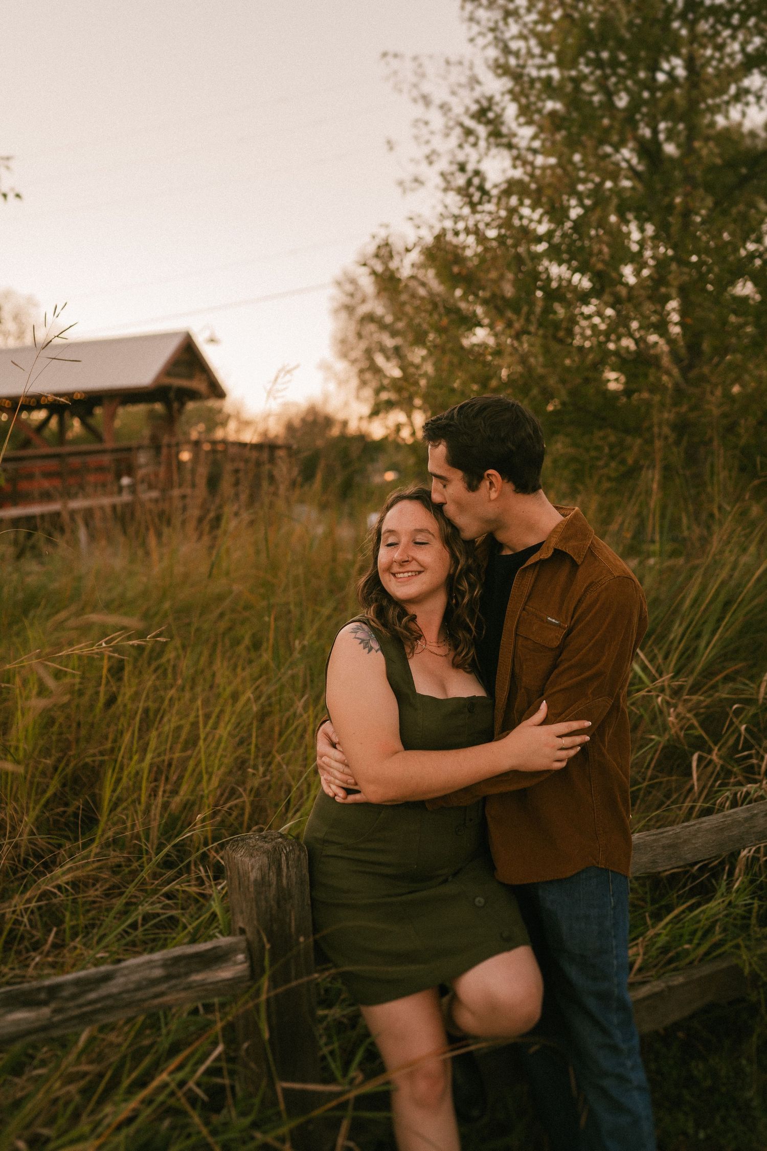 A couple shares an intimate moment by a fence during golden hour.