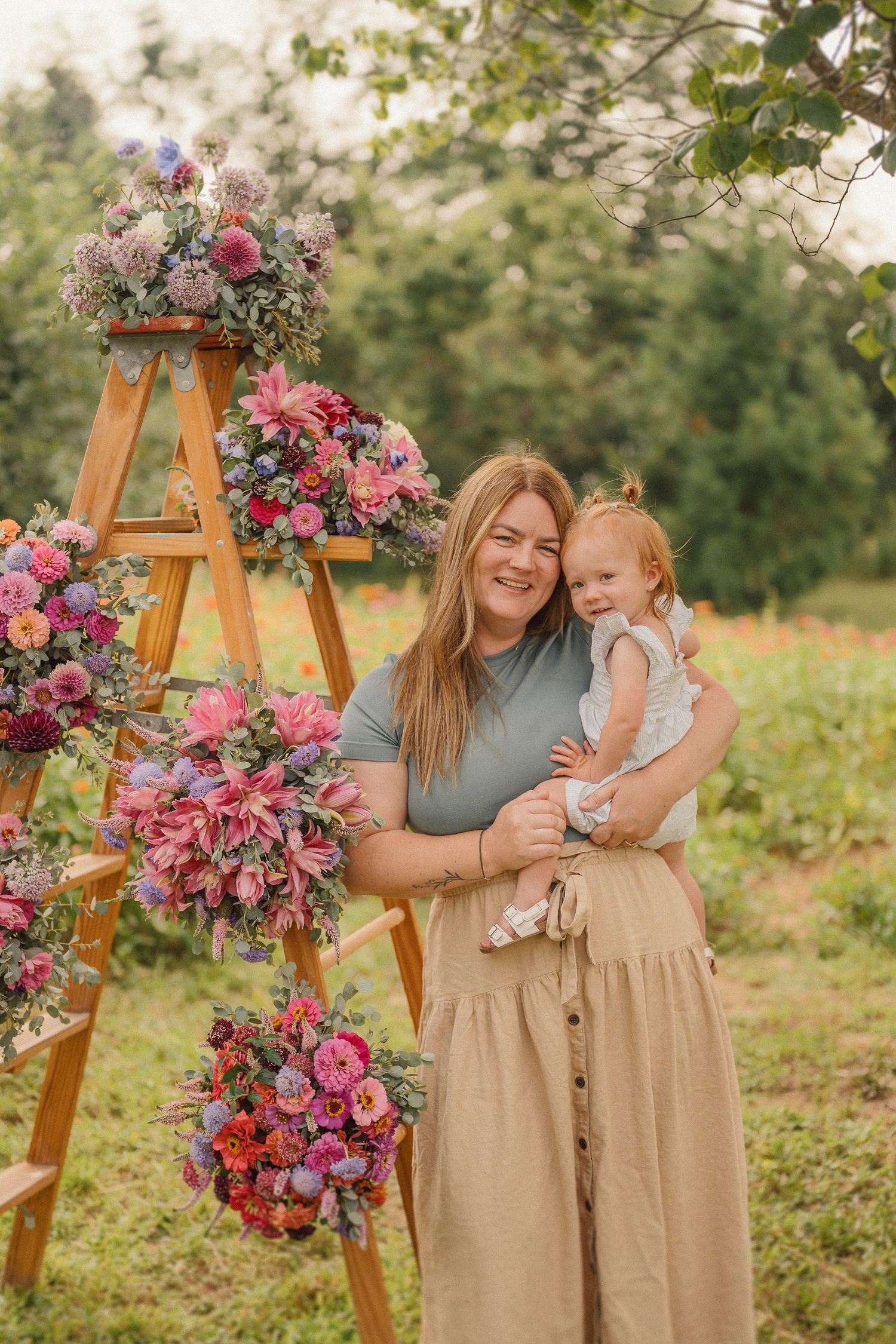 A sunny outdoor portrait featuring a floral ladder display with people smiling together in a natural garden setting.