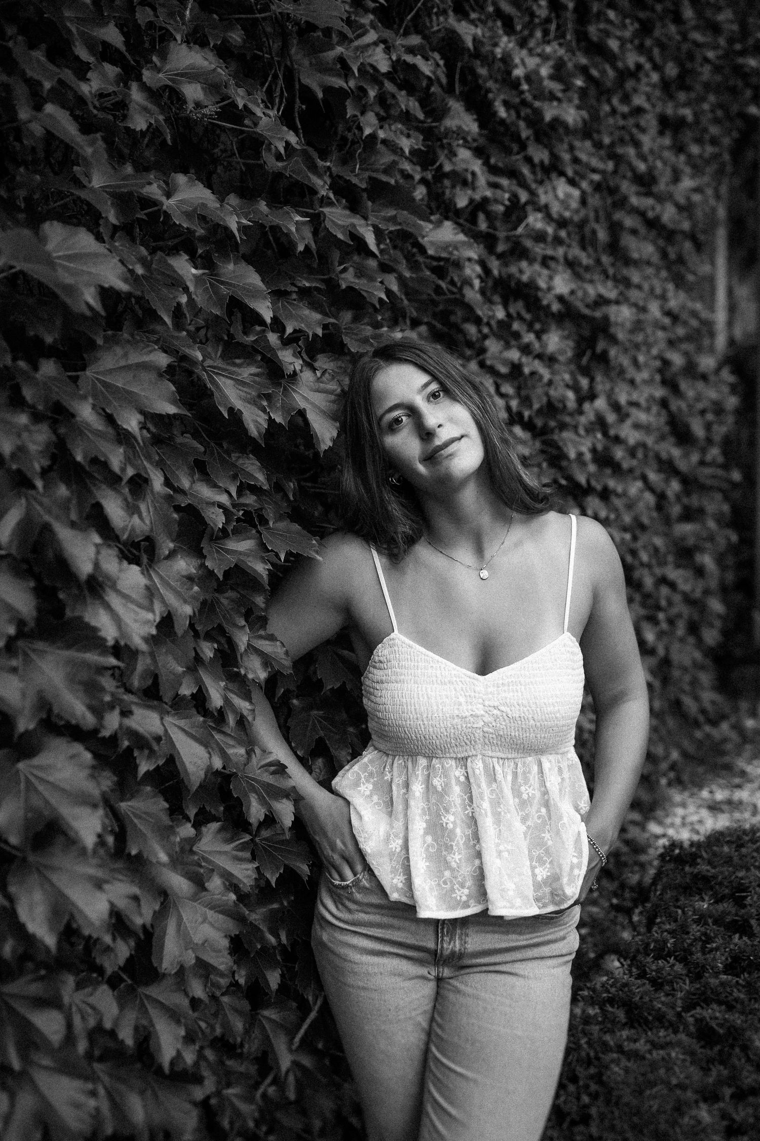 Black and white portrait against ivy-covered wall with dramatic shadows.
