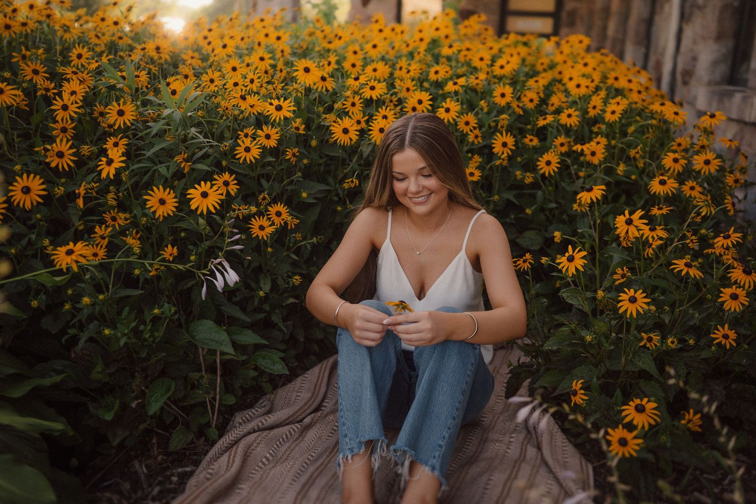Person sitting among vibrant black-eyed susan flowers during golden hour sunset in a garden setting.