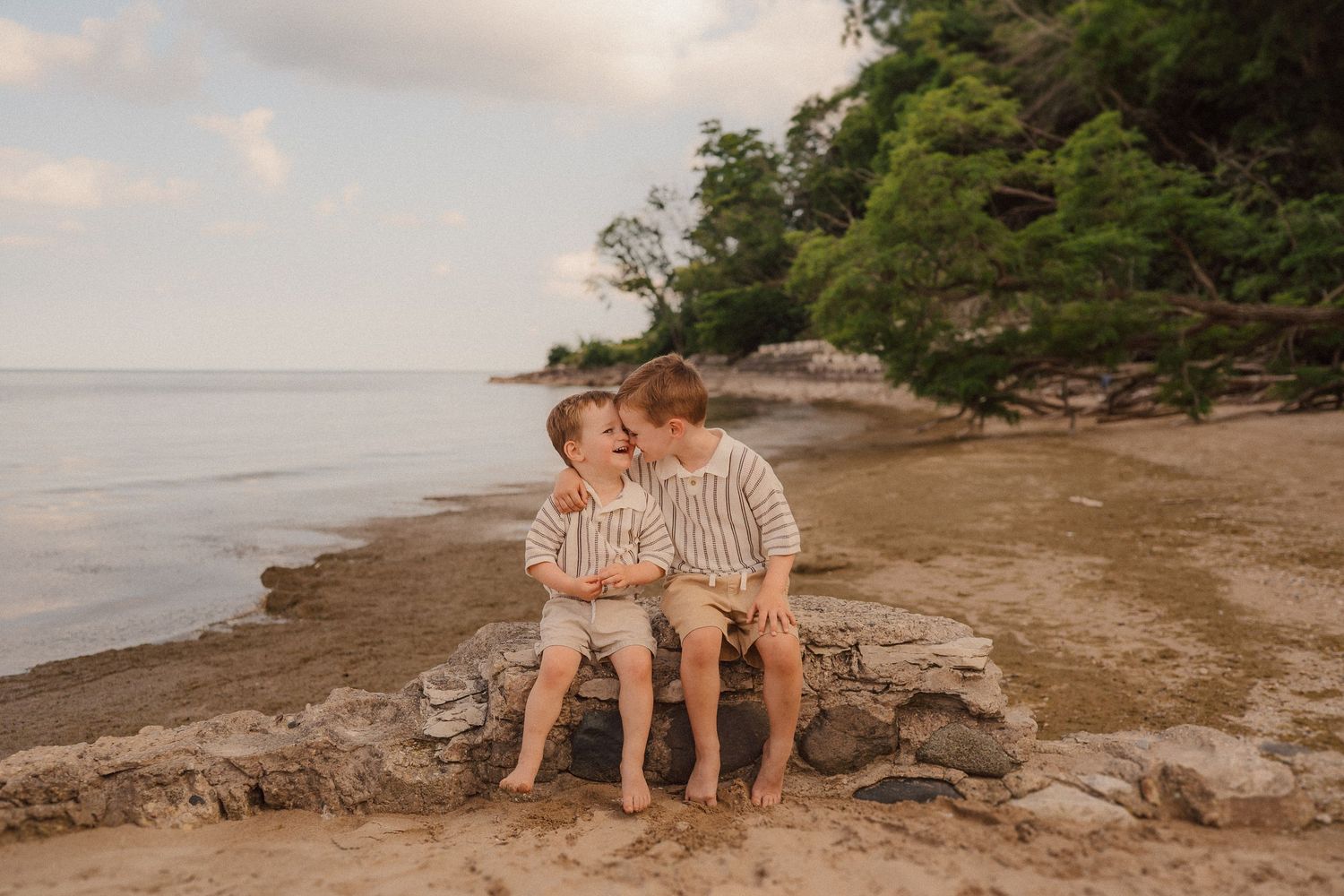 Couple sitting together on rocky beach shoreline at sunset enjoying intimate moments by the water.