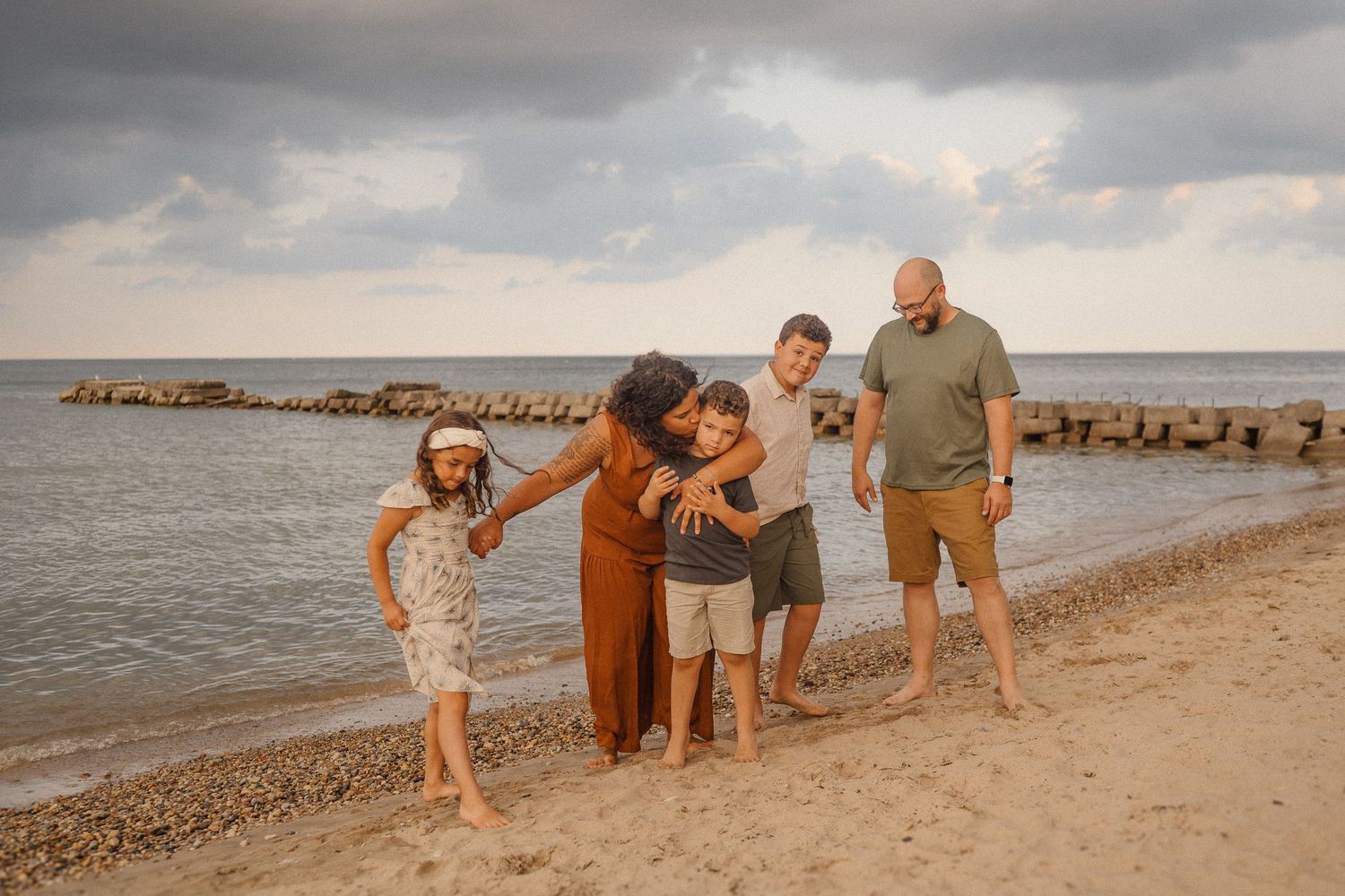 People exploring and playing on a scenic beach with rock jetties at sunset with warm golden light.