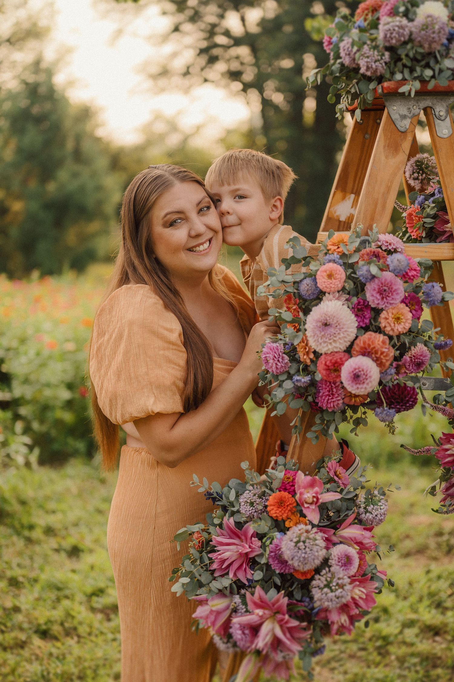 Tender moments captured near a wooden easel adorned with pink and purple florals at sunset.