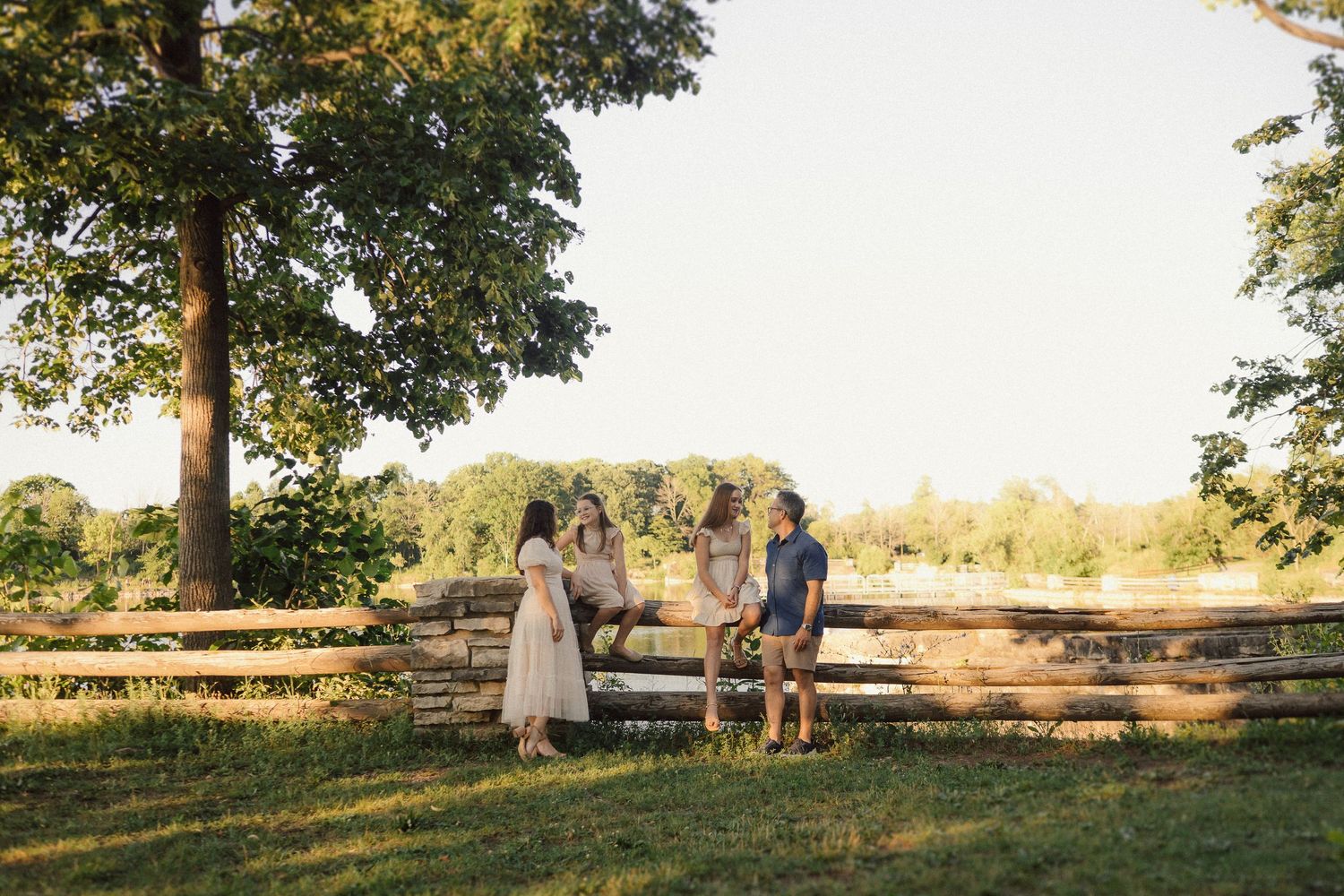 Wide landscape view of people sitting on benches near trees during golden hour.