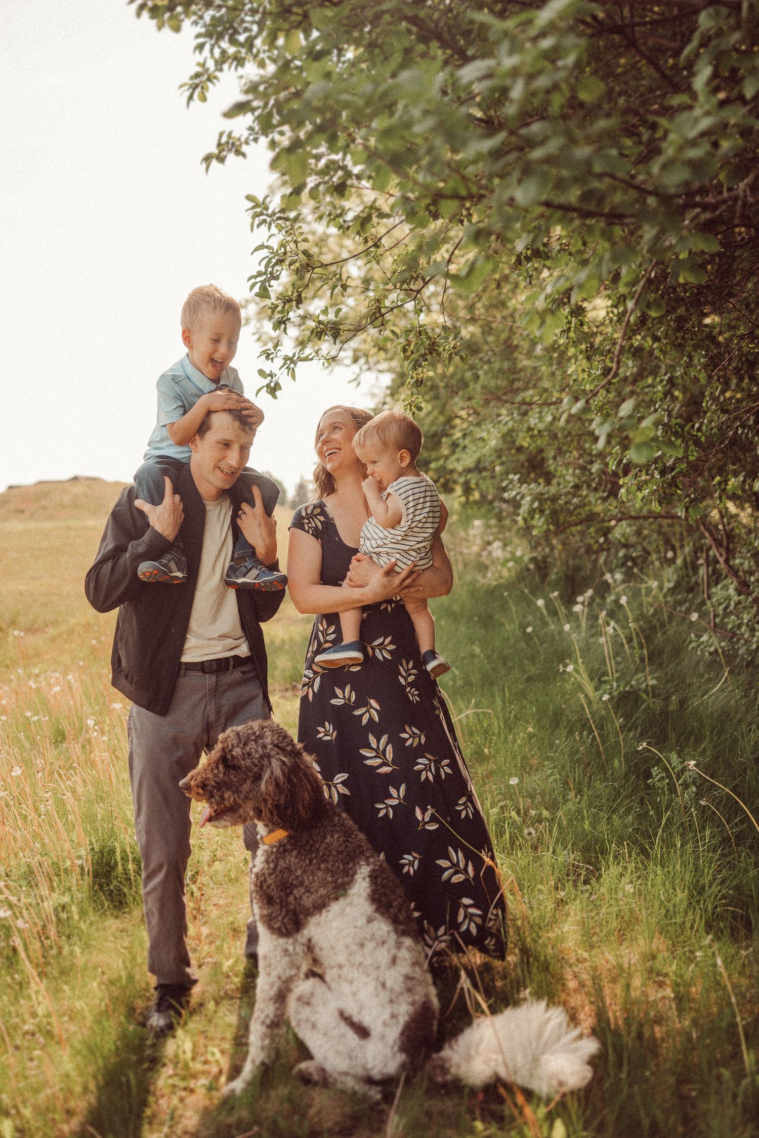 Family outdoor portrait with children and spotted dog against natural foliage.
