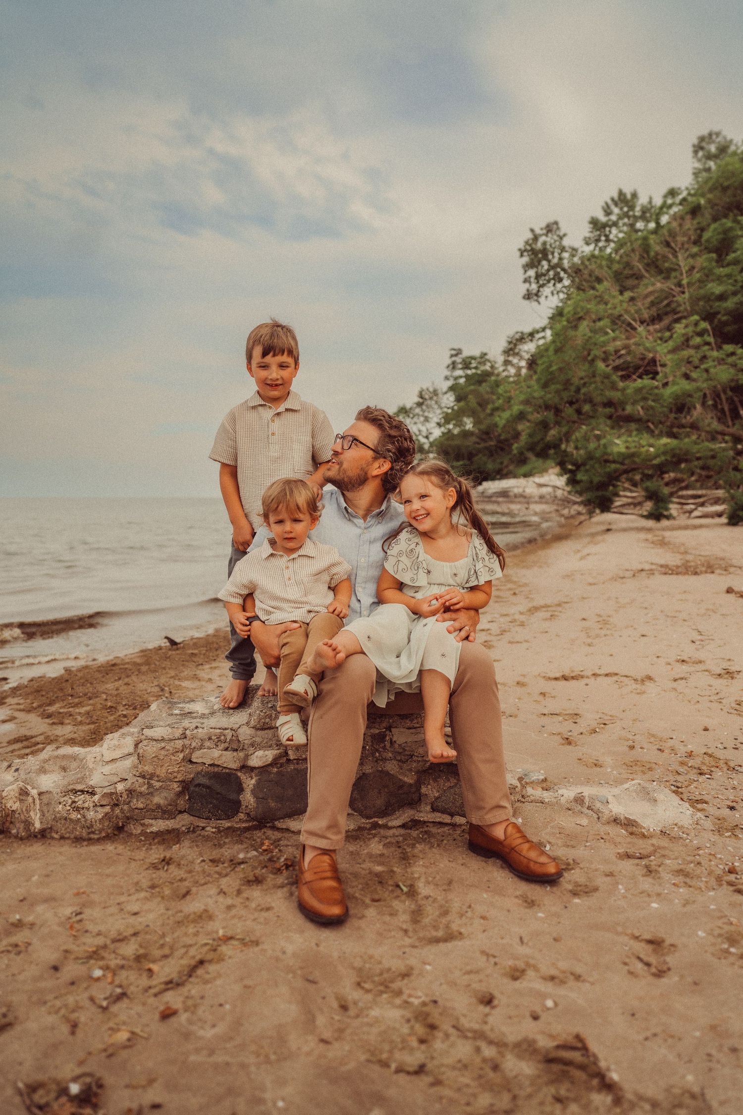 A casual family portrait captured on a rocky beach during sunset.