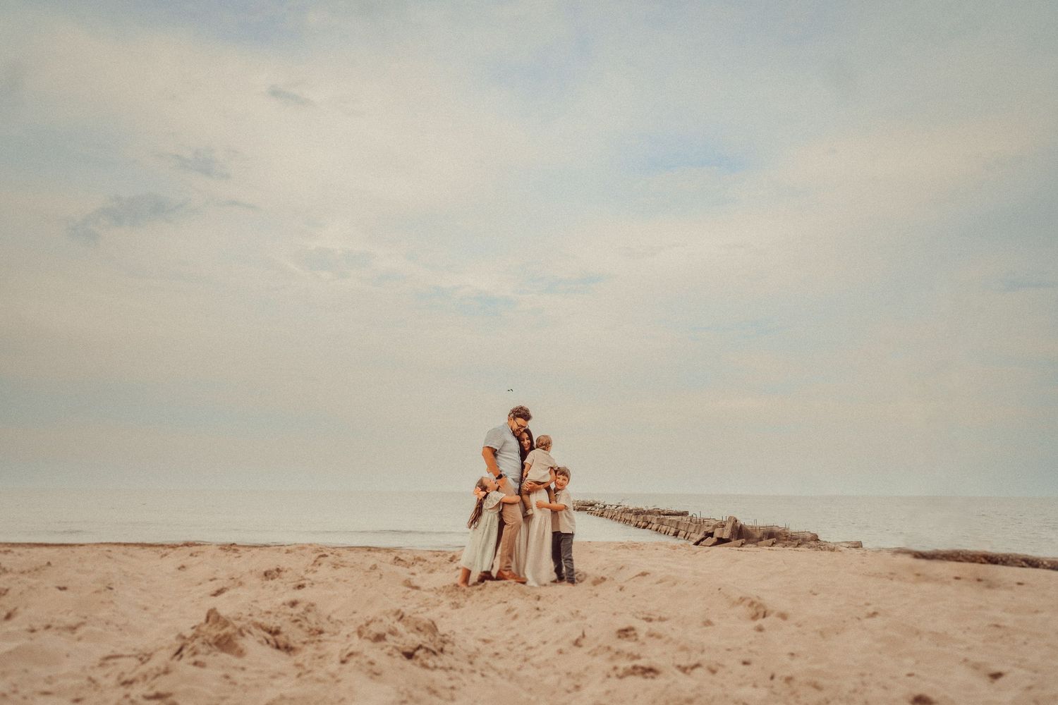 Family stands together on sandy beach against cloudy sky.