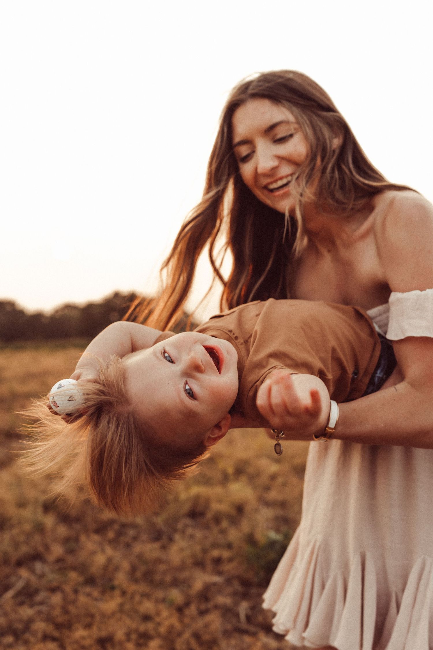 A playful moment between parent and child against a sunset backdrop in a field.