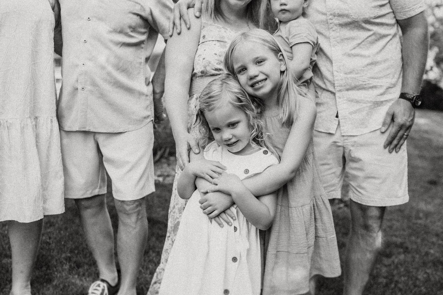 Close-up black and white portrait of children embracing while standing on grass.