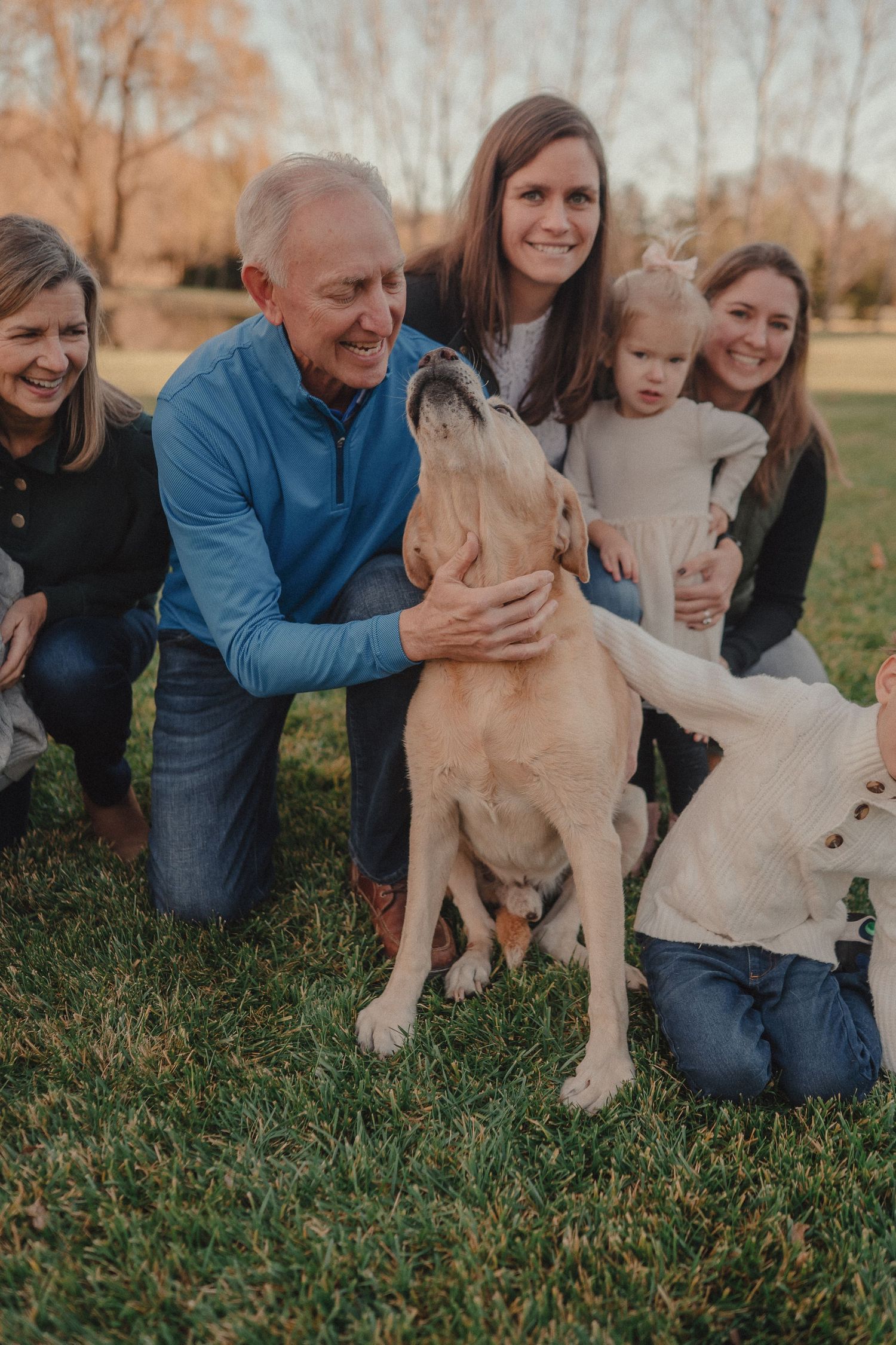 Family members sitting in grass playing with their golden retriever puppy during an outdoor photoshoot.