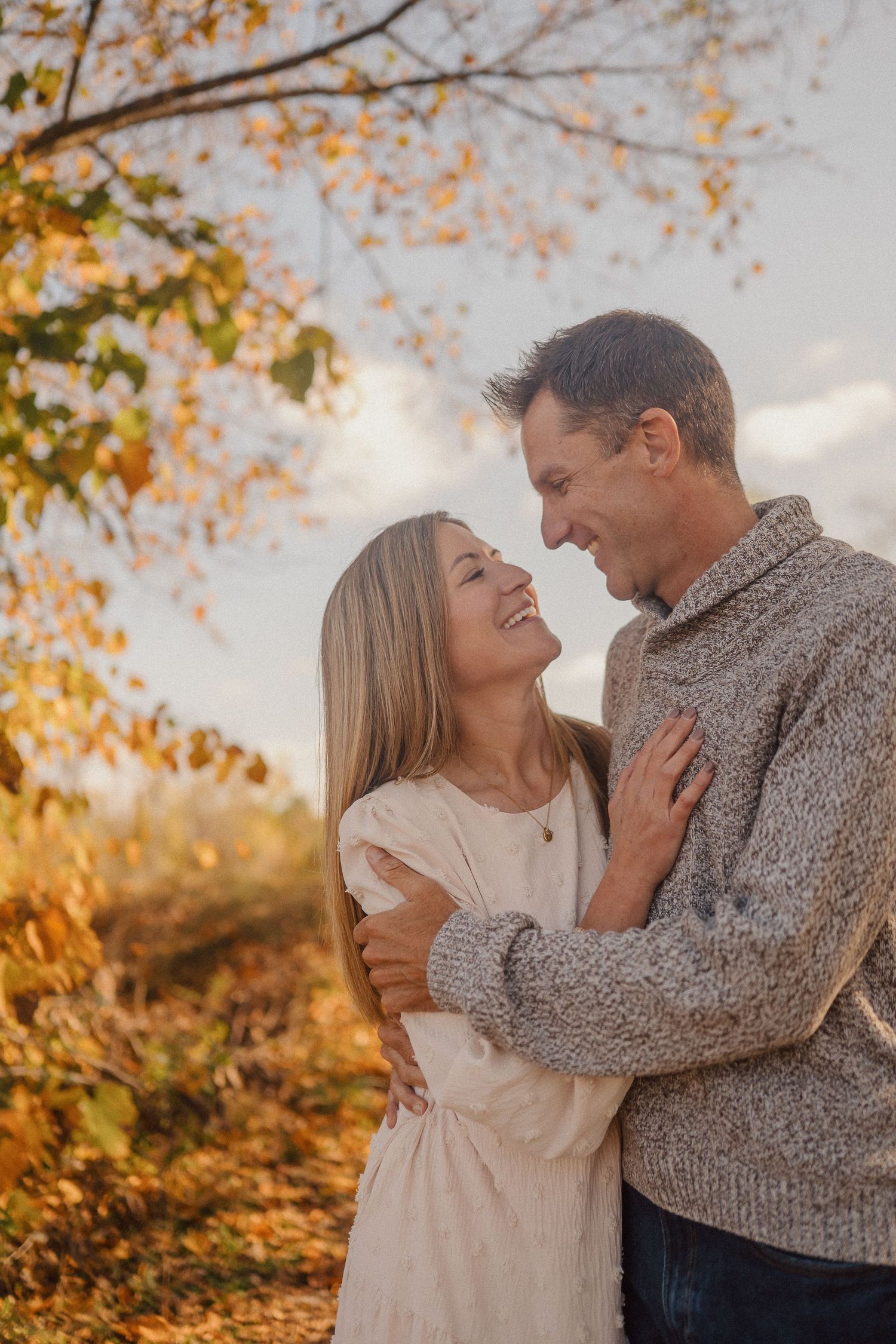 A couple shares intimate laughs while embracing outdoors in cozy sweaters during fall.