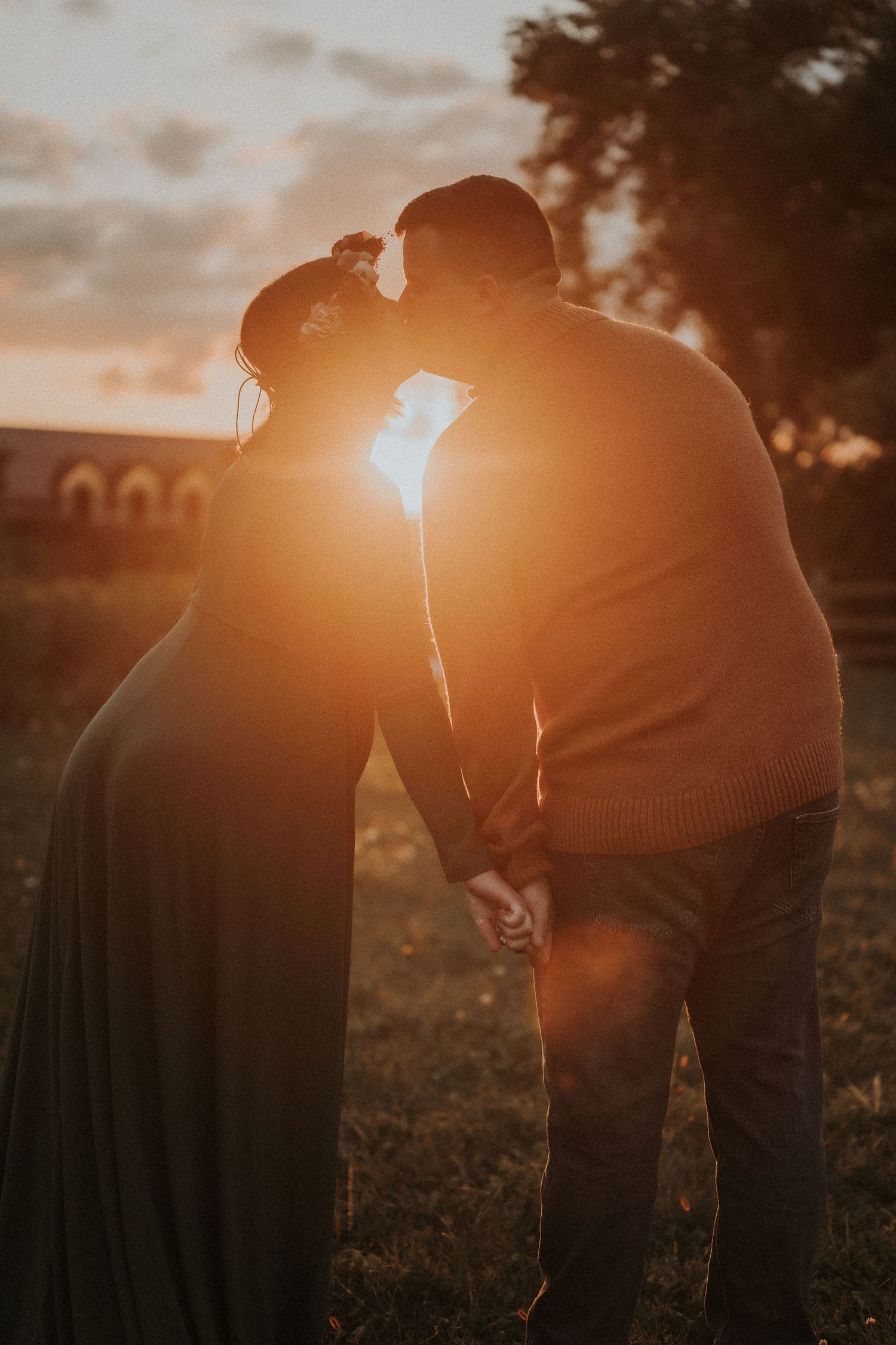 Silhouetted couple sharing intimate moment against dramatic sunset.
